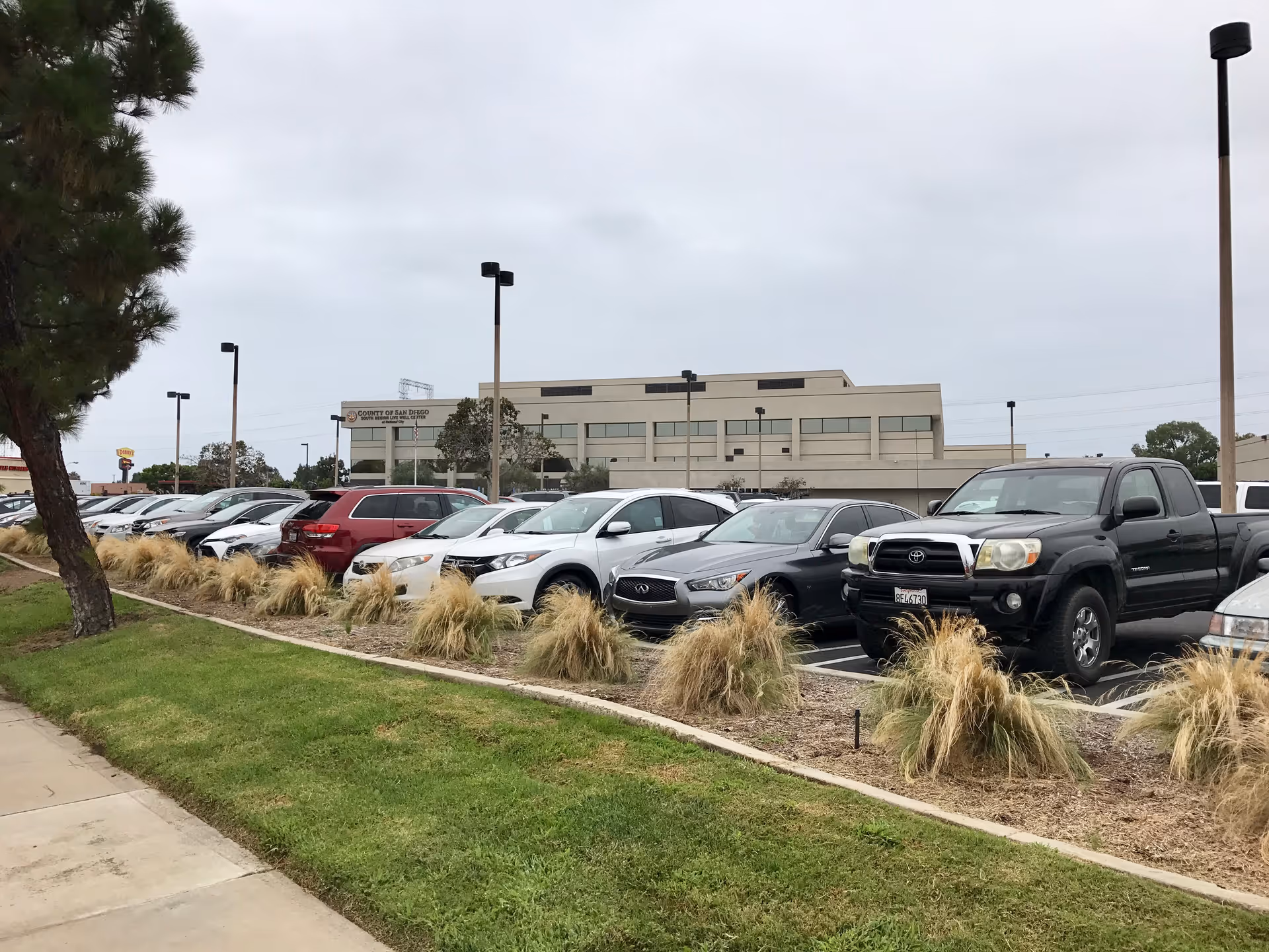 Parking lot in front of a beige office building with landscaped medians and tall light posts.