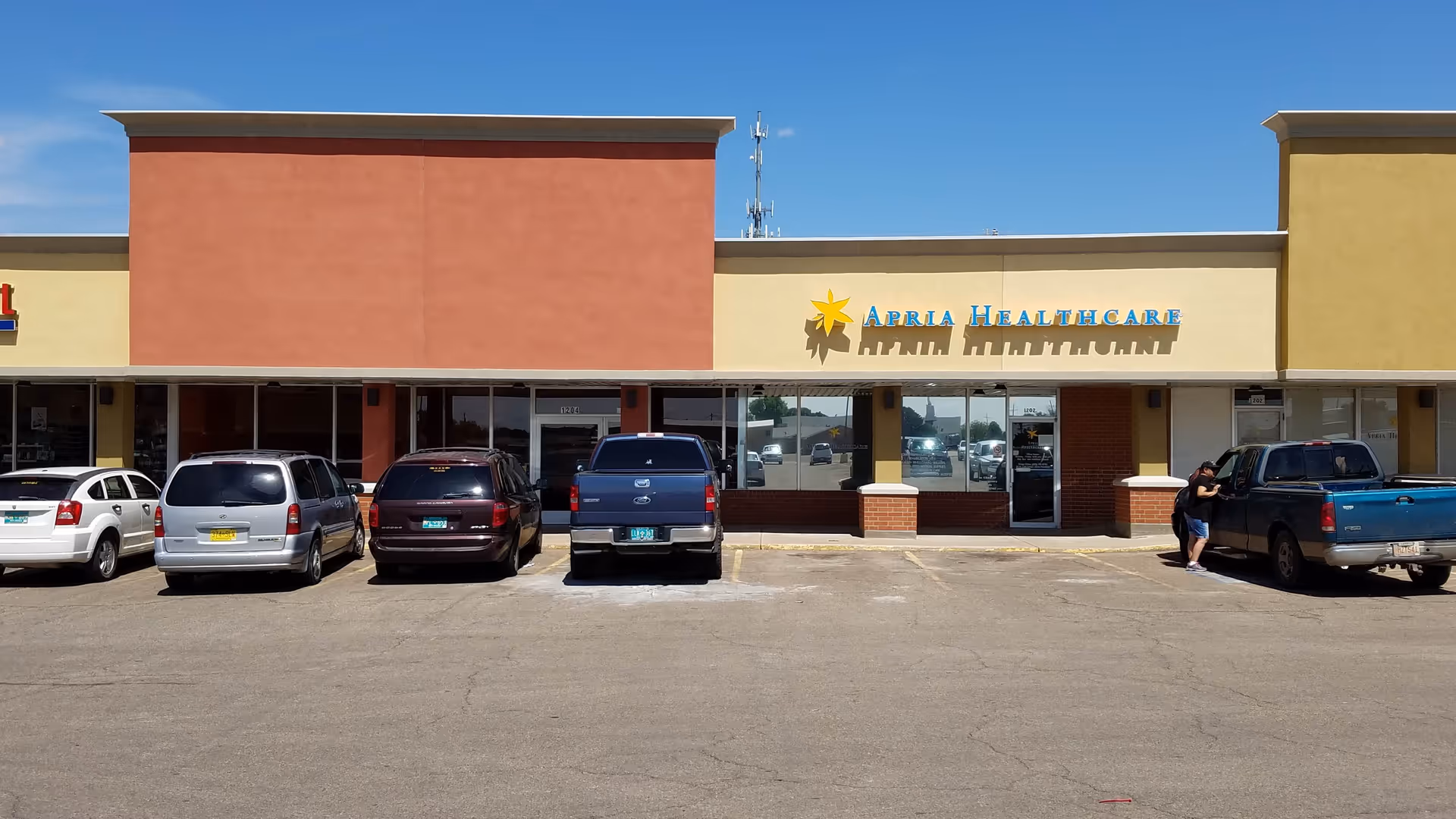 Exterior view of Apria Healthcare storefront with parked cars in front.