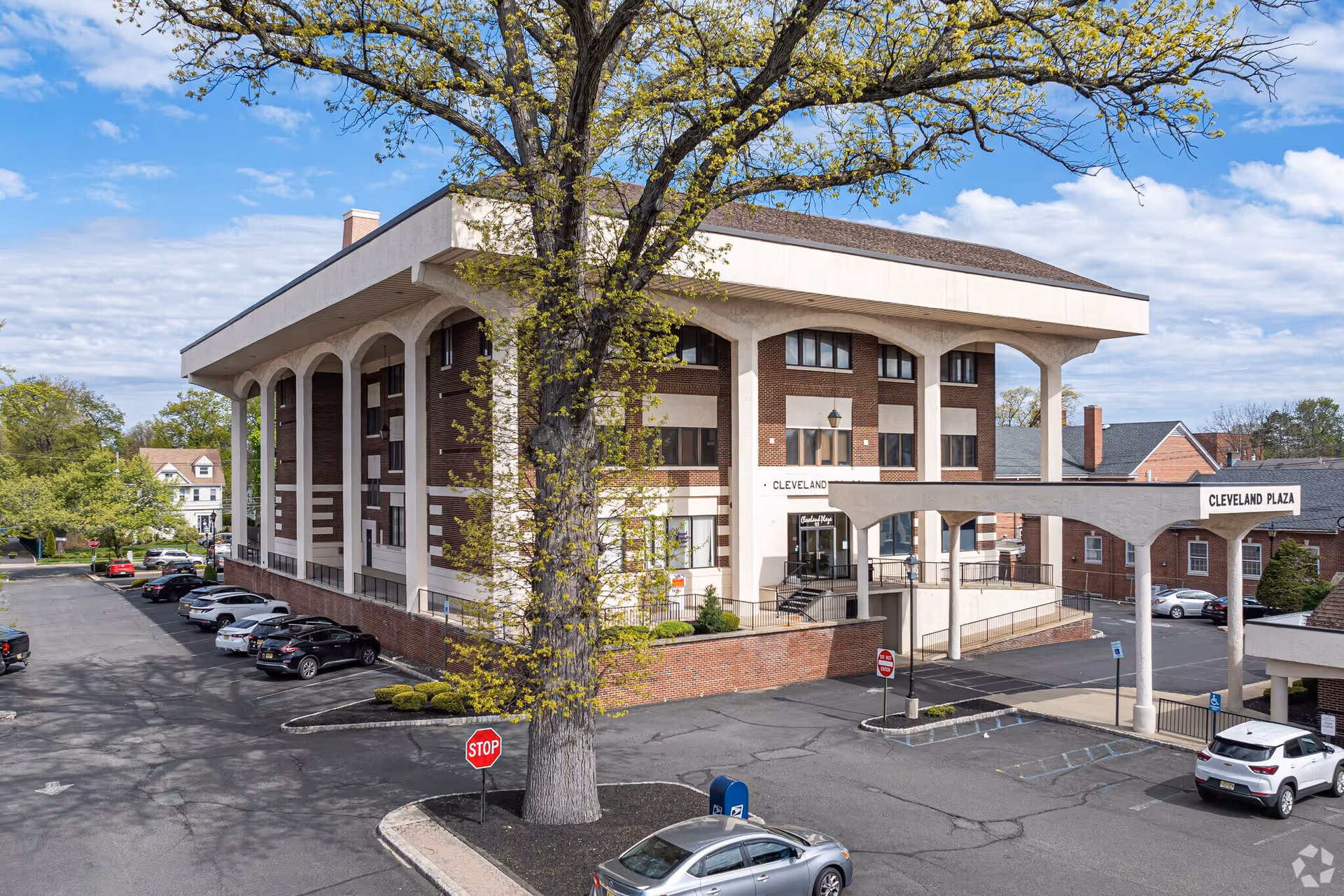 A large two-story facility with arches, a driveway, parking lot, and a tree in front.