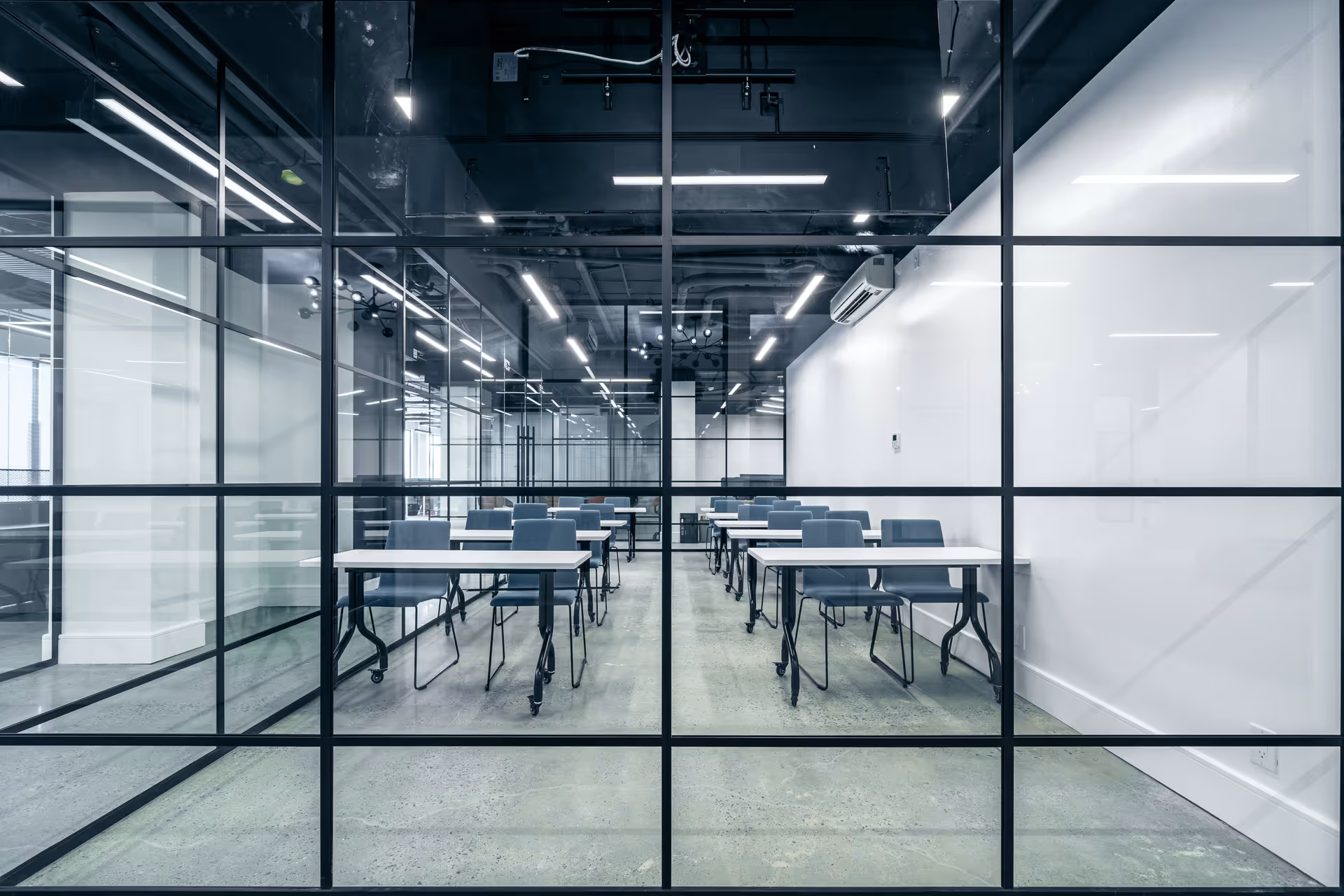 Glass-walled conference room with rows of blue chairs and white tables.