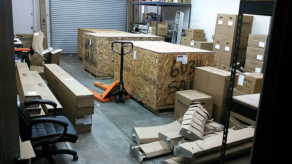 Warehouse storage area with large crates, boxes, pallets, and shelving.