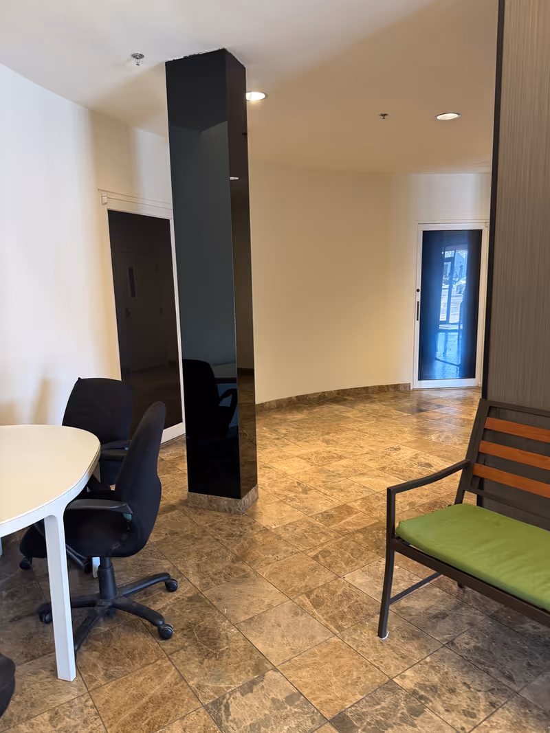 Indoor reception area with a round white table, black chairs, and a green-cushioned bench.