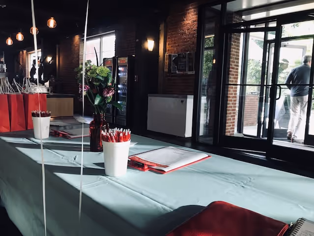 Indoor lobby area with a long teal table, pens, flowers, and gift bags near the entrance.