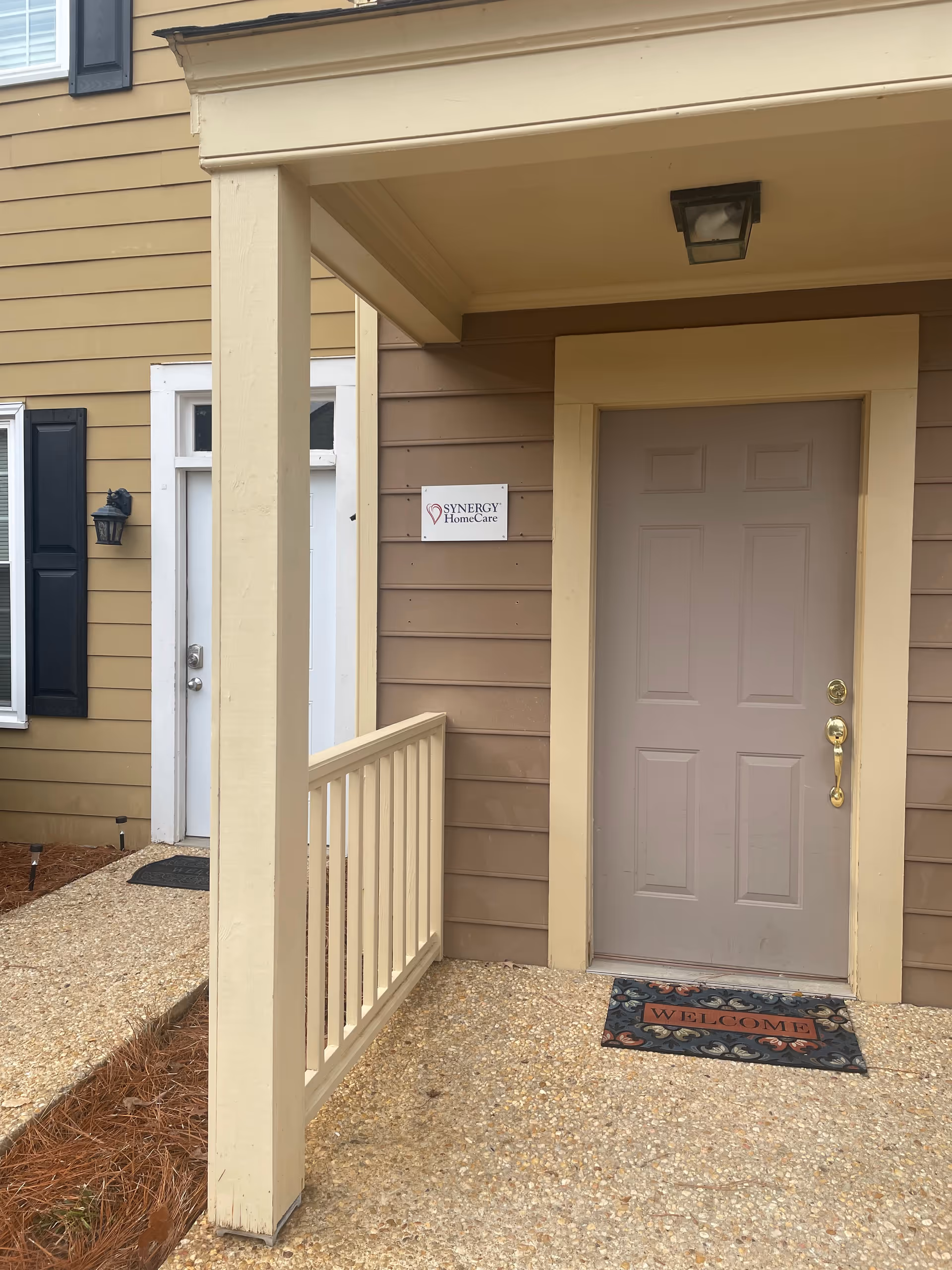 Front entrance of a building with Synergy HomeCare sign and welcome mat.
