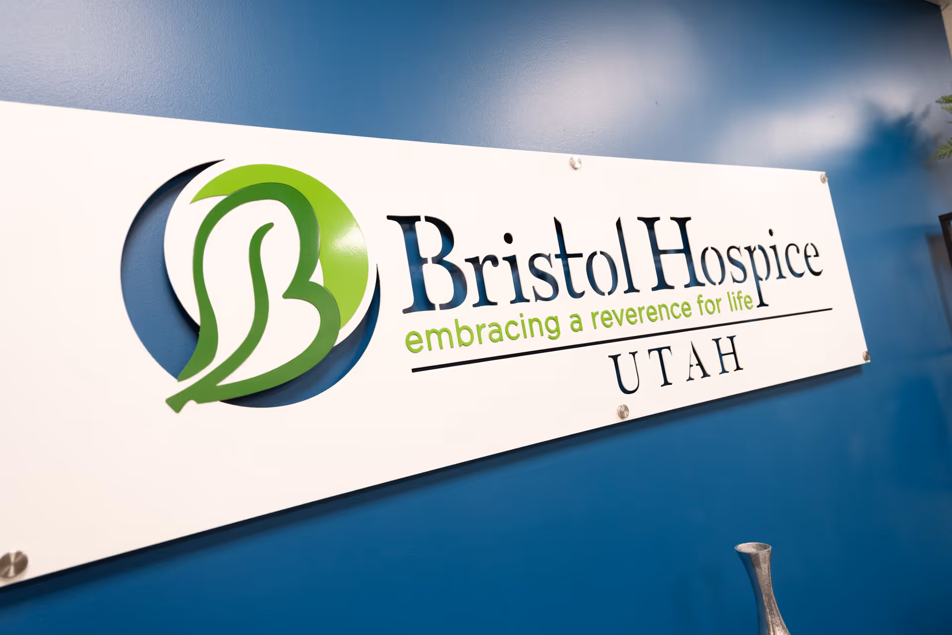 White Bristol Hospice Utah sign with green emblem mounted on blue wall.