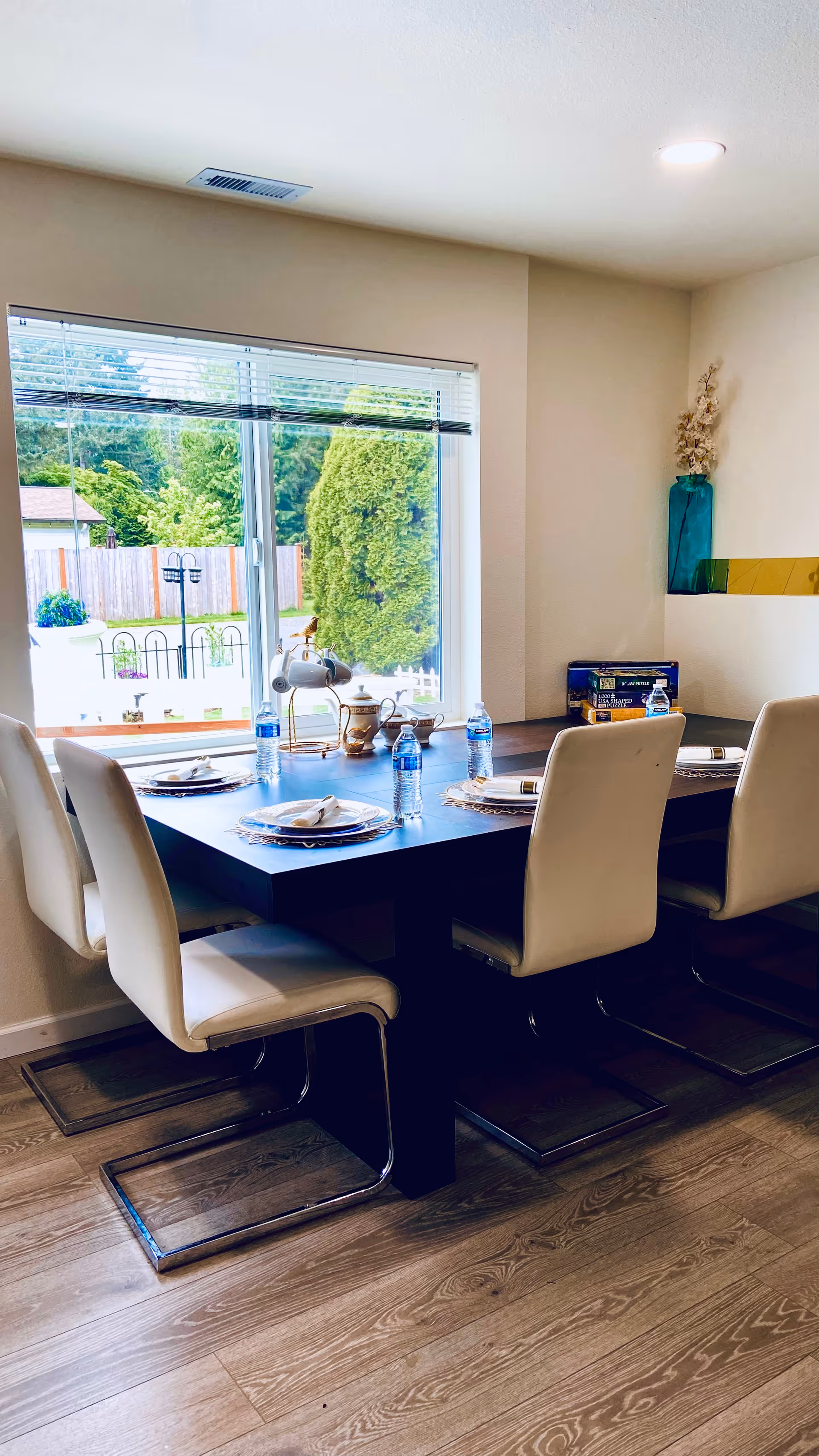 Sunlit dining room with a long table set for a meal and water bottles.