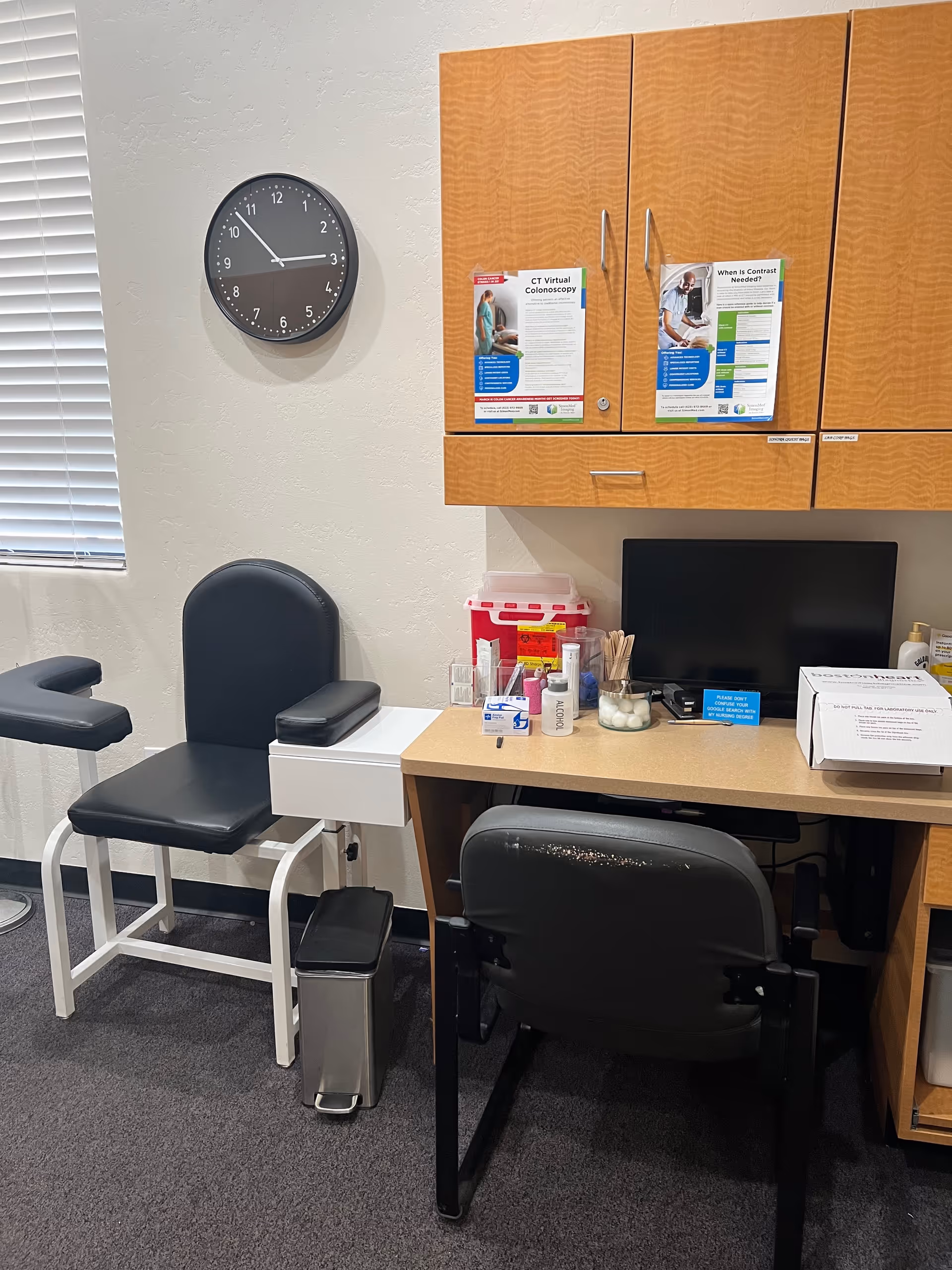 Clinic exam area with chair, desk, cabinets, clock, and medical supplies.
