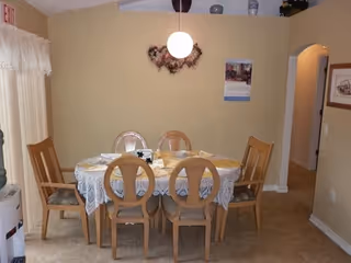 Round dining table with six wooden chairs in a beige-walled dining room.