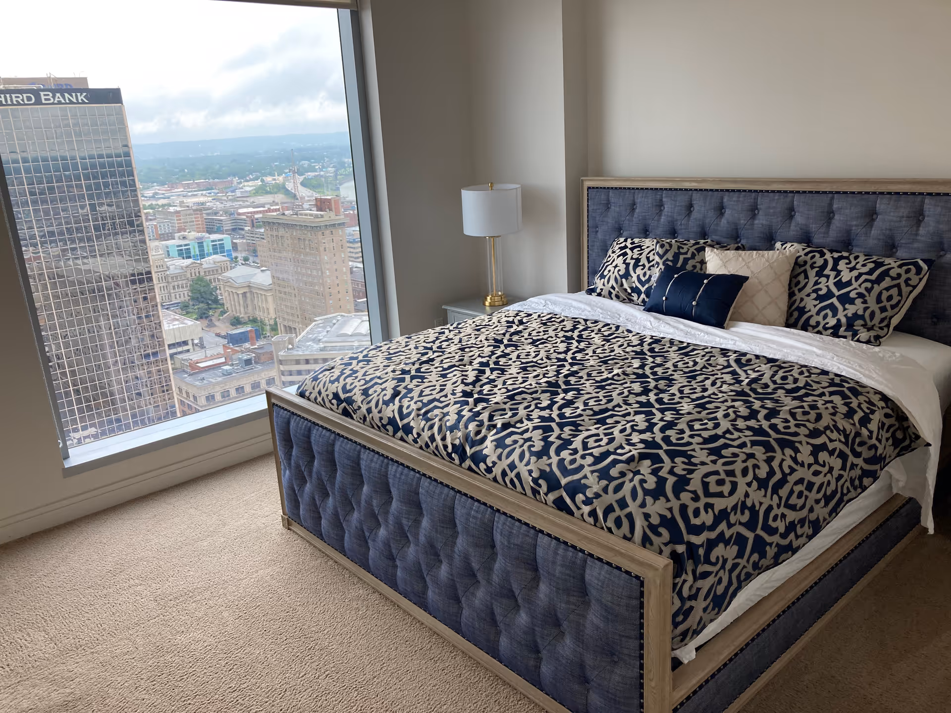 A blue upholstered bed with patterned bedding in a high-rise bedroom.