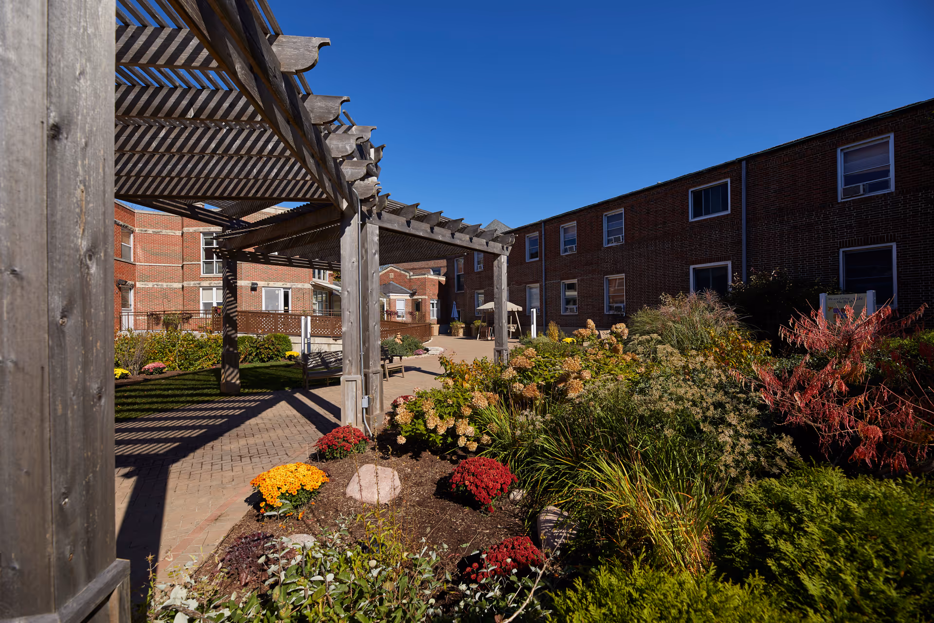 Outdoor courtyard with brick buildings, a wooden pergola, and colorful flower beds.