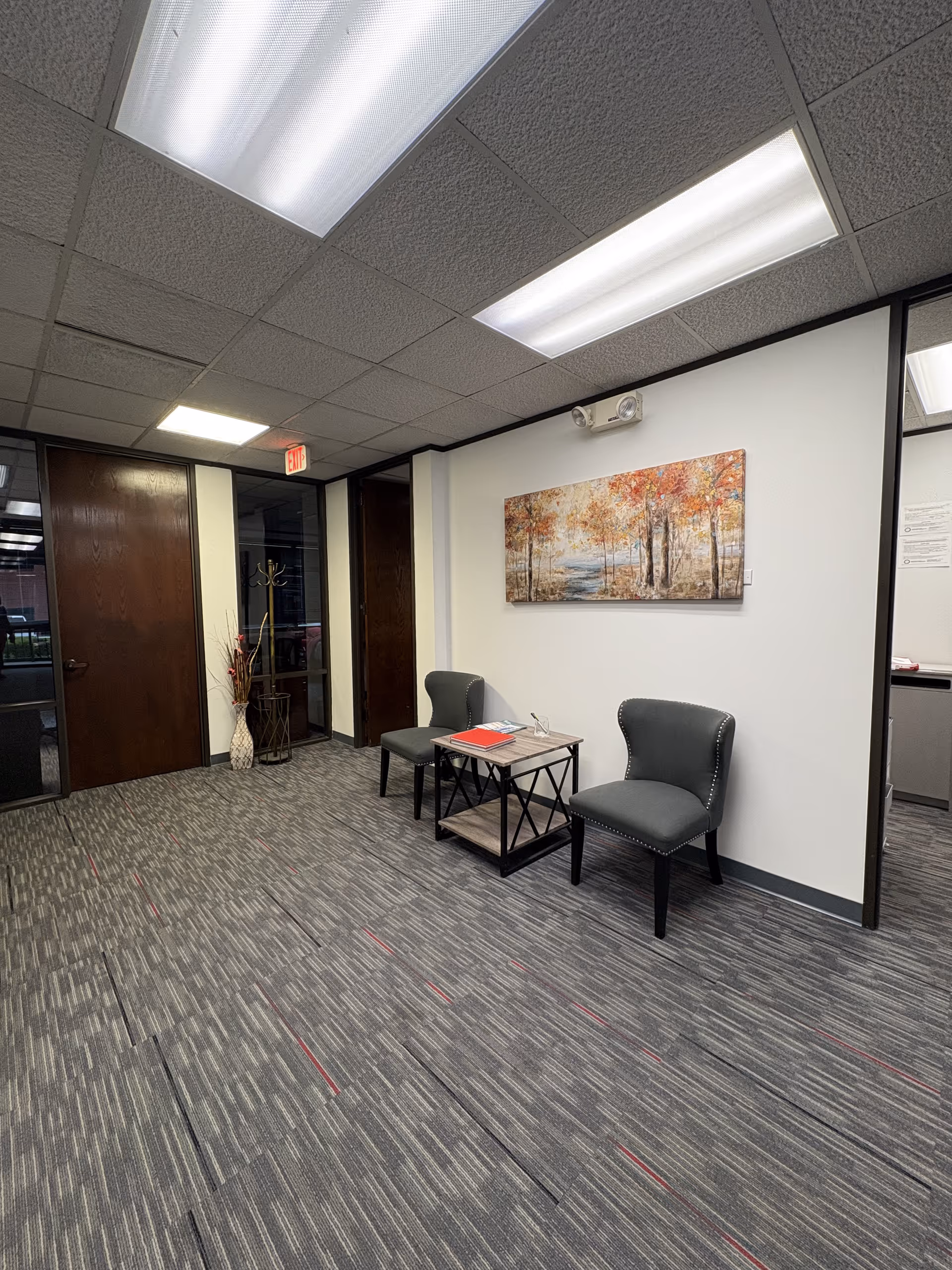 A small waiting area with two chairs, a coffee table, and wall art in a corridor.