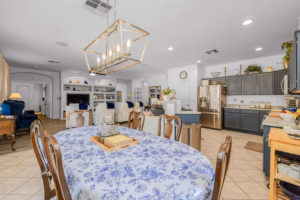 A spacious, airy senior living common area with a round dining table and kitchen in view.