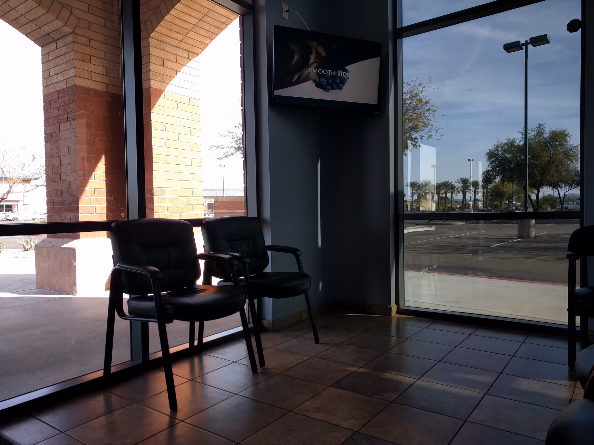 Interior waiting area with two black chairs by large windows overlooking the parking lot.