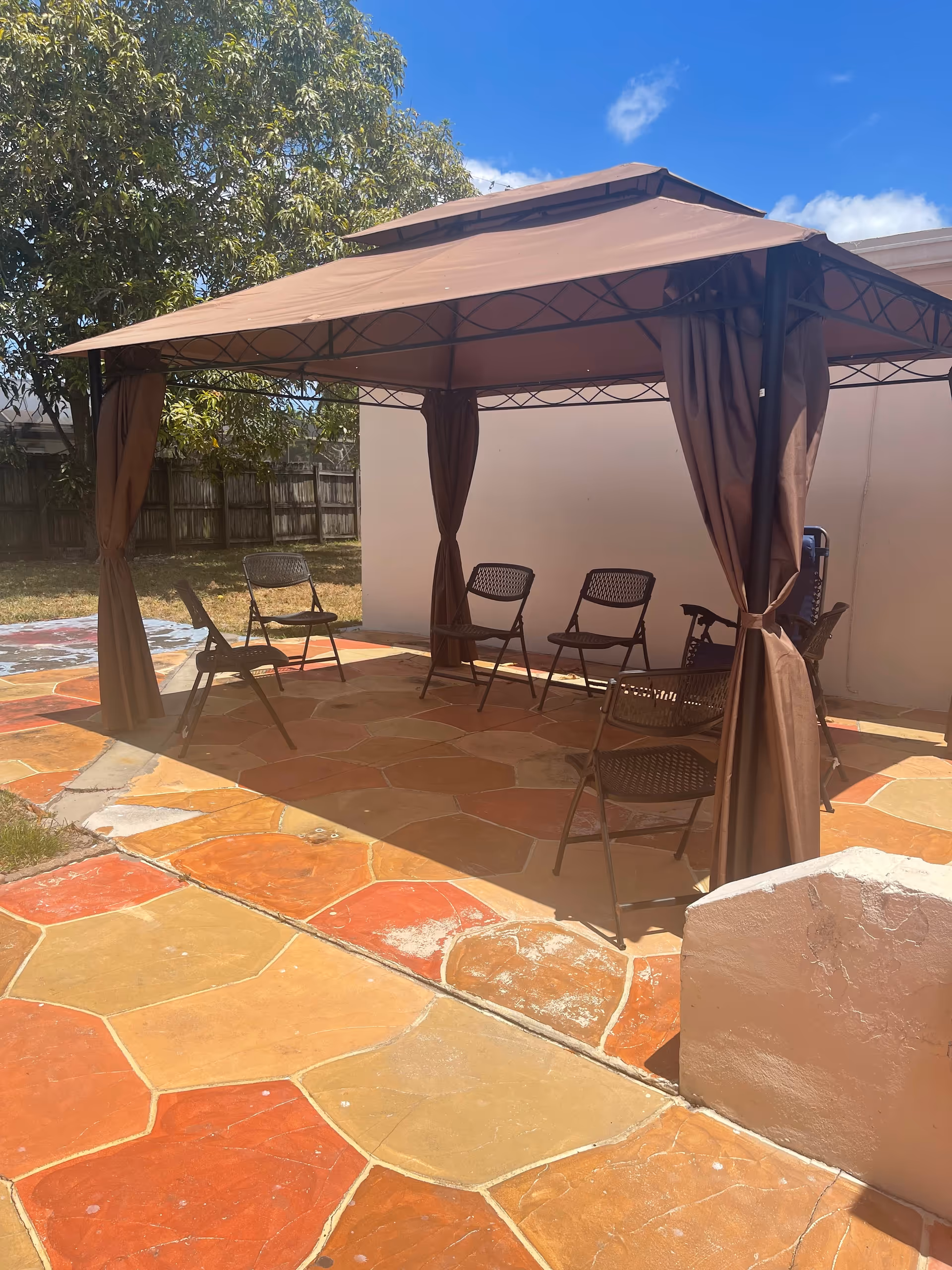 Outdoor seating area under a brown canopy with brown curtains and several chairs.