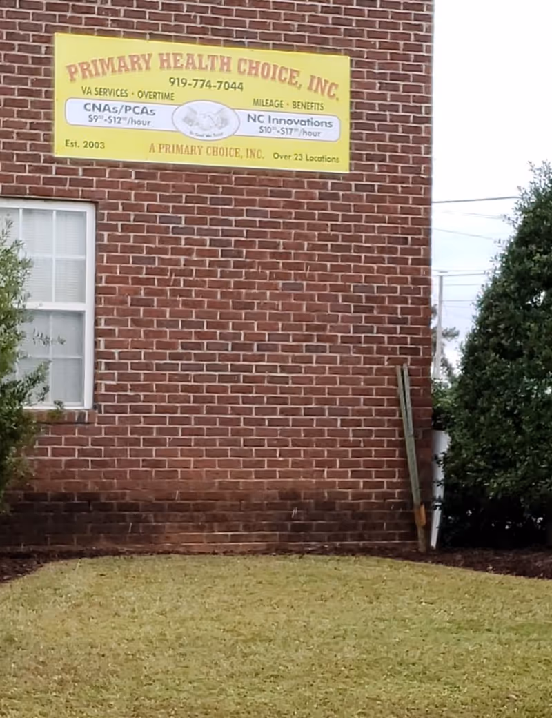 Brick building exterior with a yellow Primary Health Choice sign and surrounding lawn.