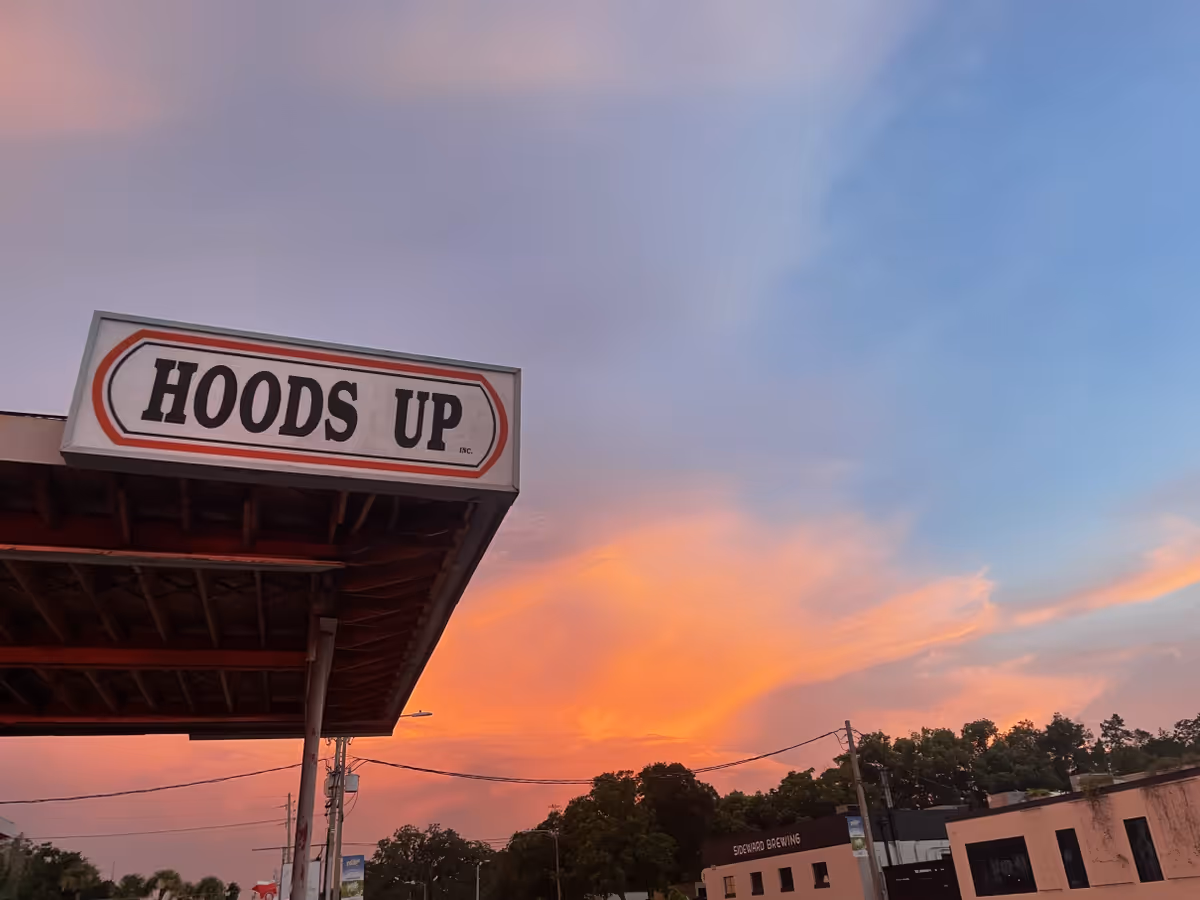 Exterior view of a building with a HOODS UP sign against a sunset sky.