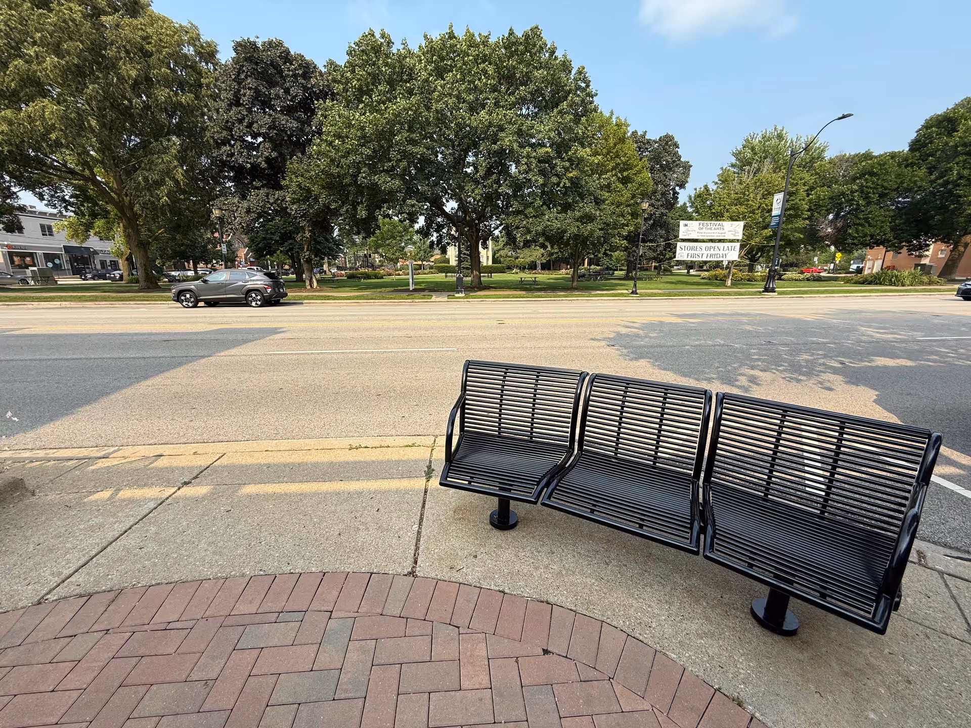 Outdoor metal bench on a sidewalk with trees and a street in the background