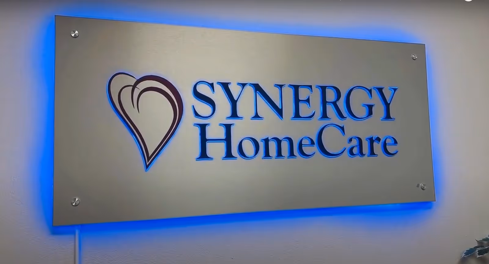 Interior wall sign reading SYNERGY HomeCare with blue-lit heart logo.
