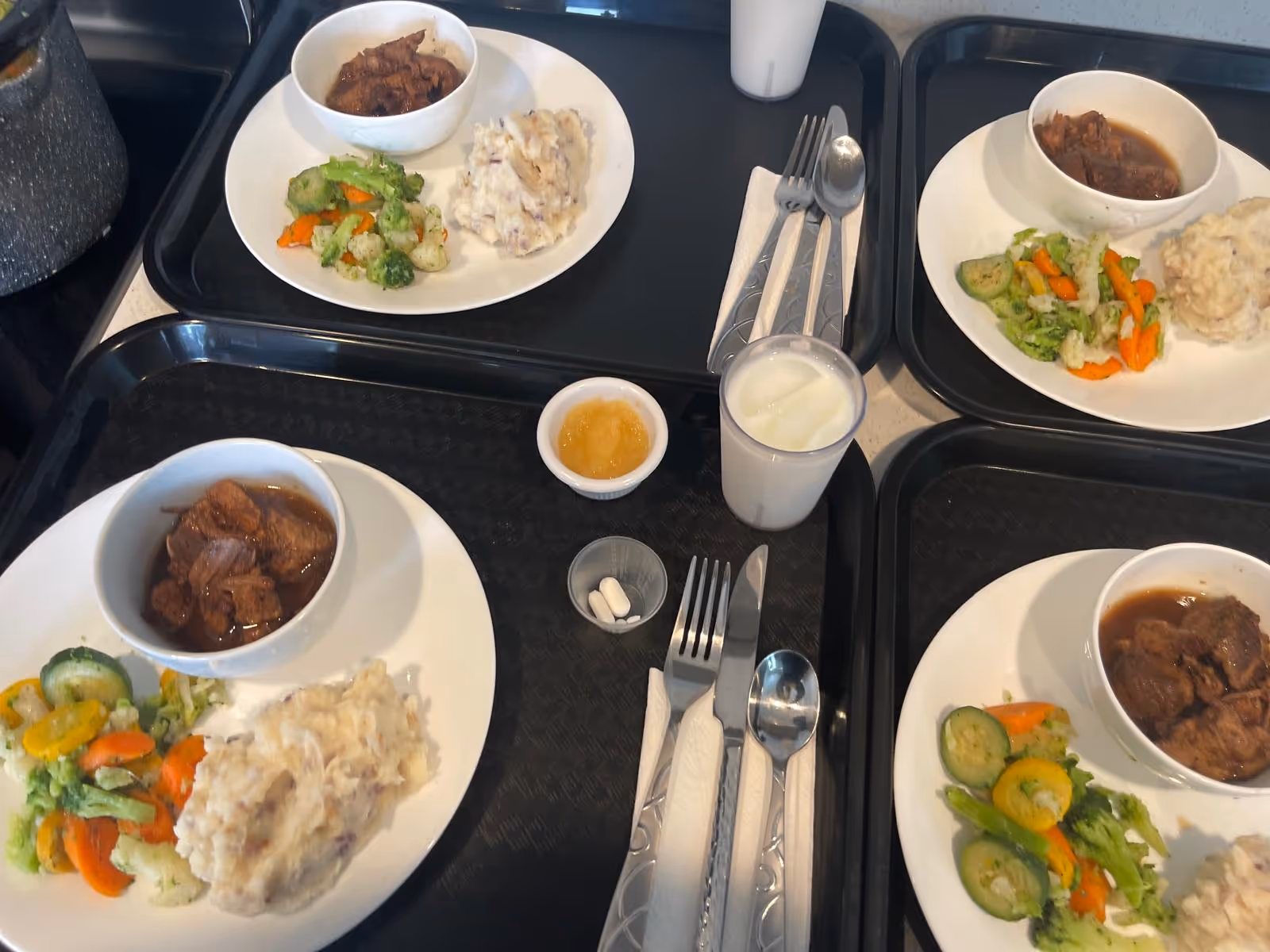 Meal trays with vegetables and stew on a dining table in a senior living facility.