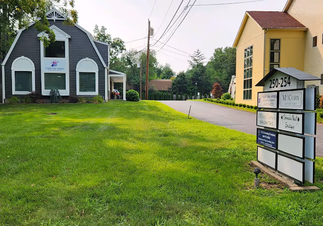 Exterior view of a green lawn, two buildings, and a roadside sign.