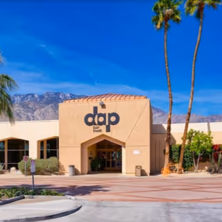 Front of a DAP Health facility with palm trees and clear blue sky.