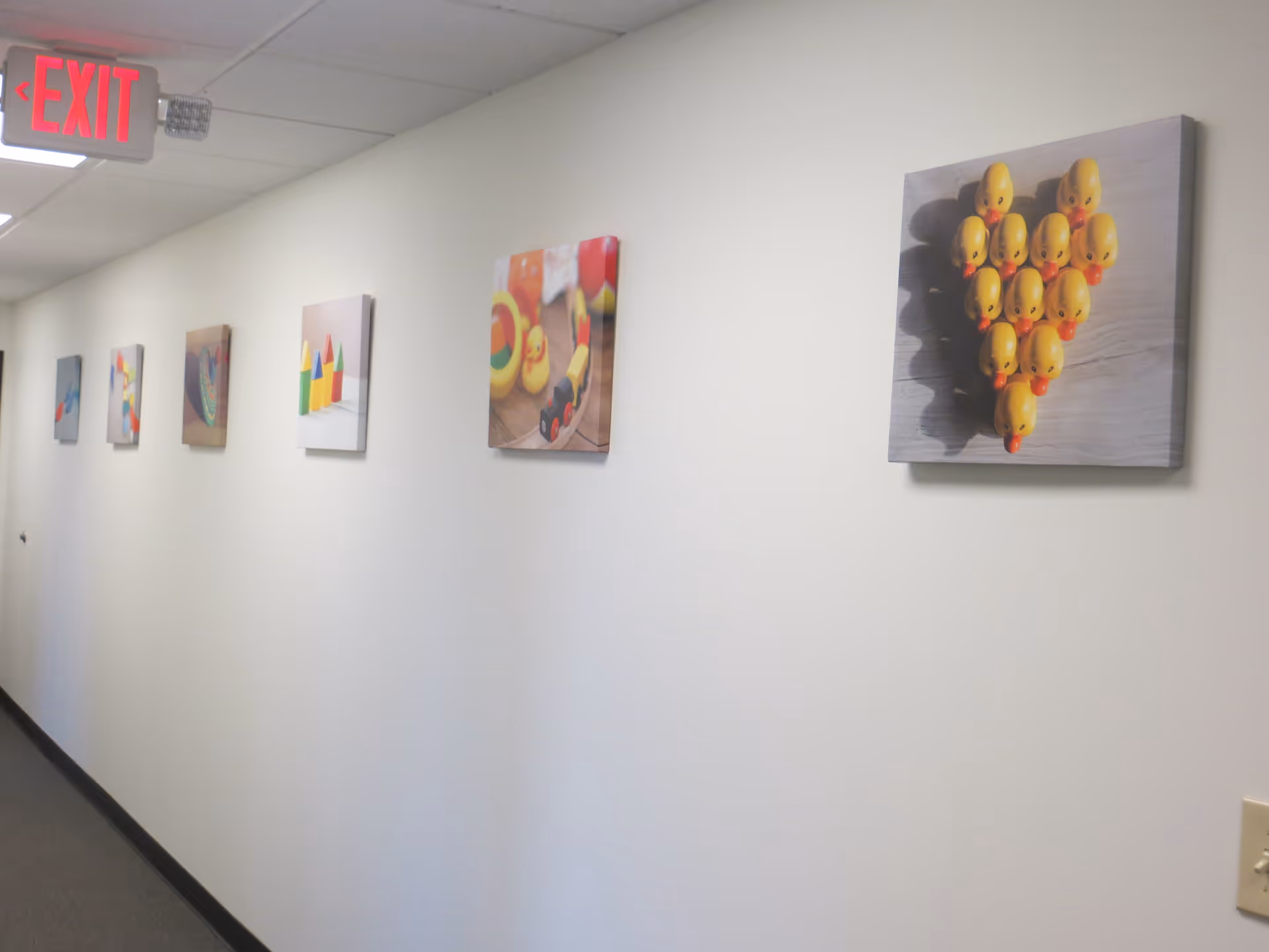 Interior corridor with an exit sign and wall-mounted framed artwork.