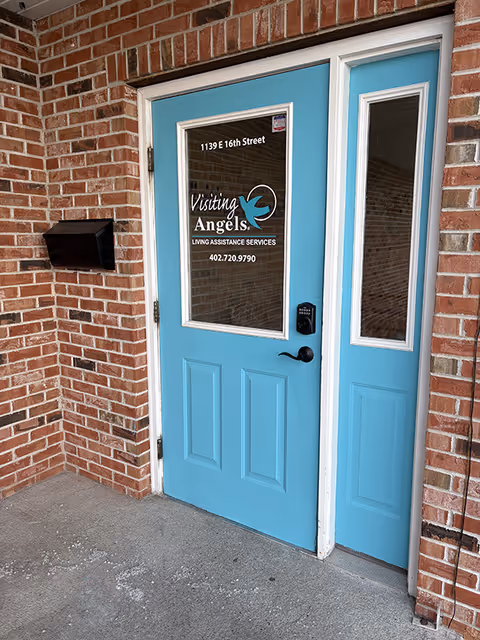 Blue entrance door with Visiting Angels signage on brick exterior wall