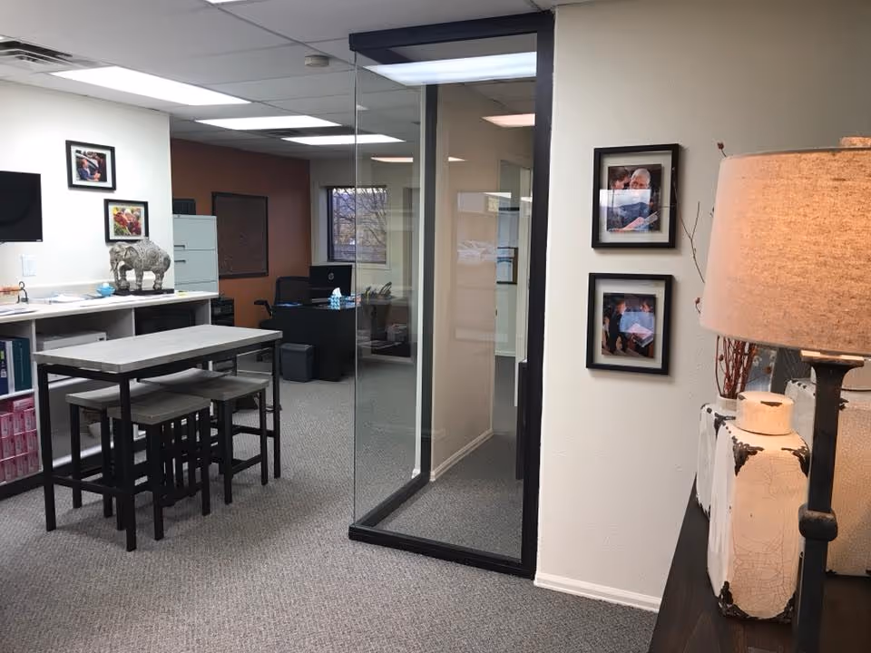 Interior office-like common area with a high table, stools, glass partition, and framed photos.