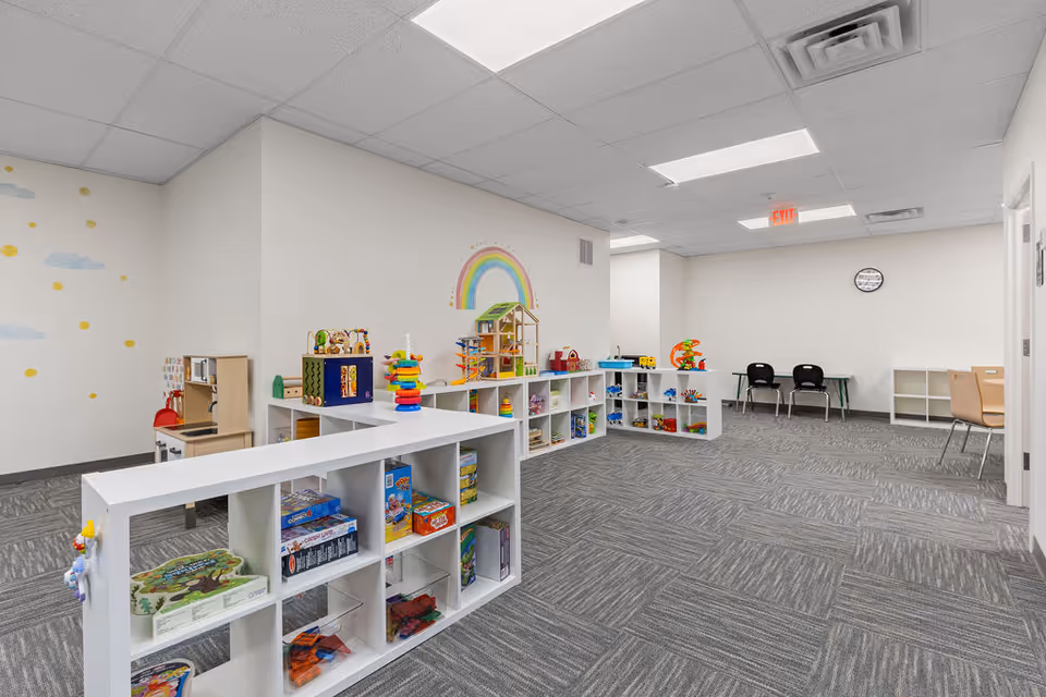 Bright play room with white cubbies, toys, a rainbow mural, and seating.