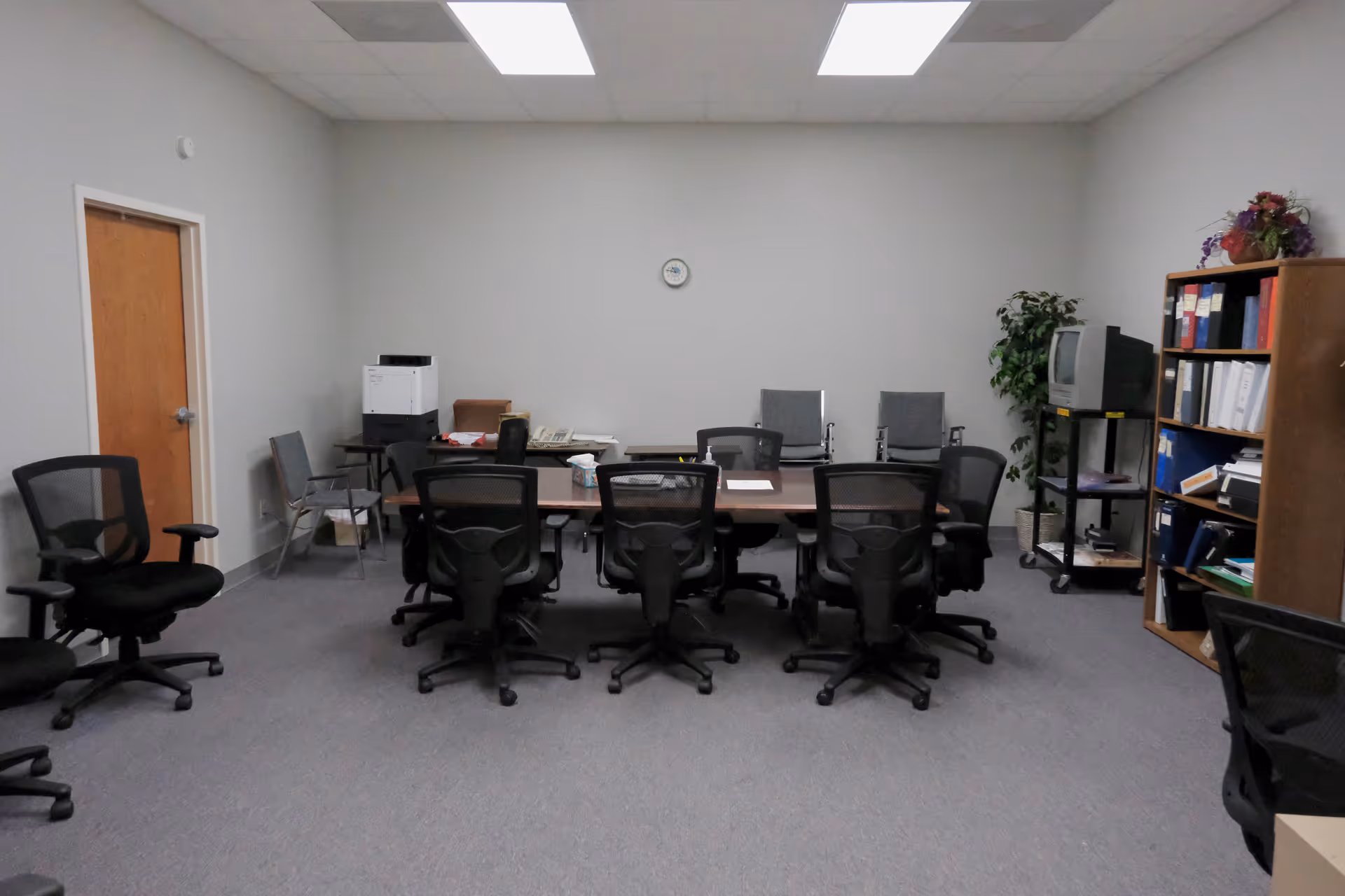 An empty conference room with a long table, many chairs, and shelving.