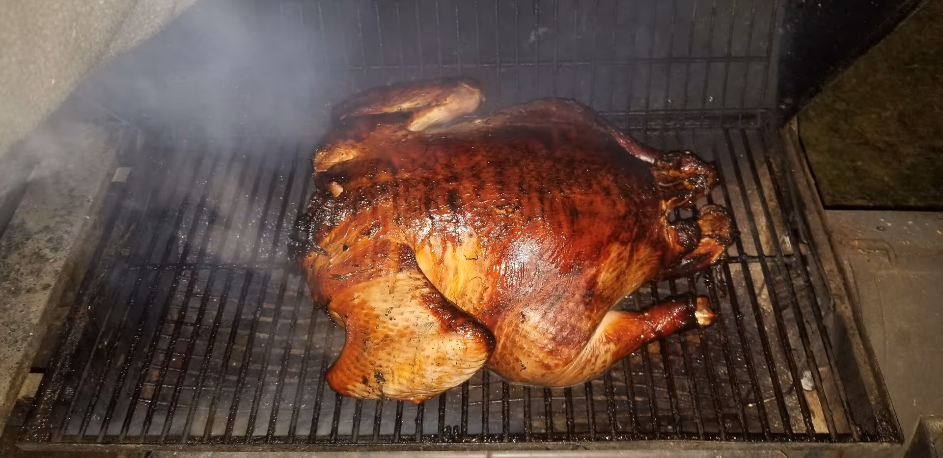 Whole roasted turkey on a grill outdoors with smoke