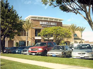 Exterior view of Barnes & Noble bookstore in a shopping plaza with parked cars.