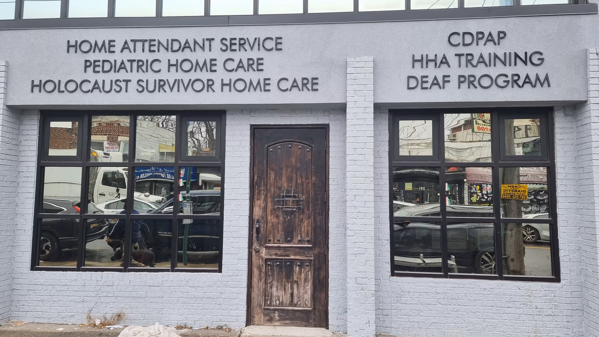 Gray storefront with wood door and large windows listing Holocaust Survivor Home Care and other services.