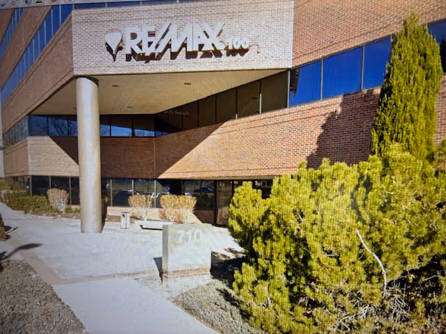 Exterior view of a brick building with a RE/MAX sign and landscaped front entrance.
