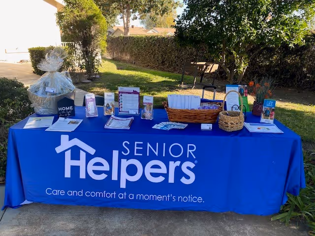 Outdoor table with Senior Helpers brochures and community materials against a sunny lawn.