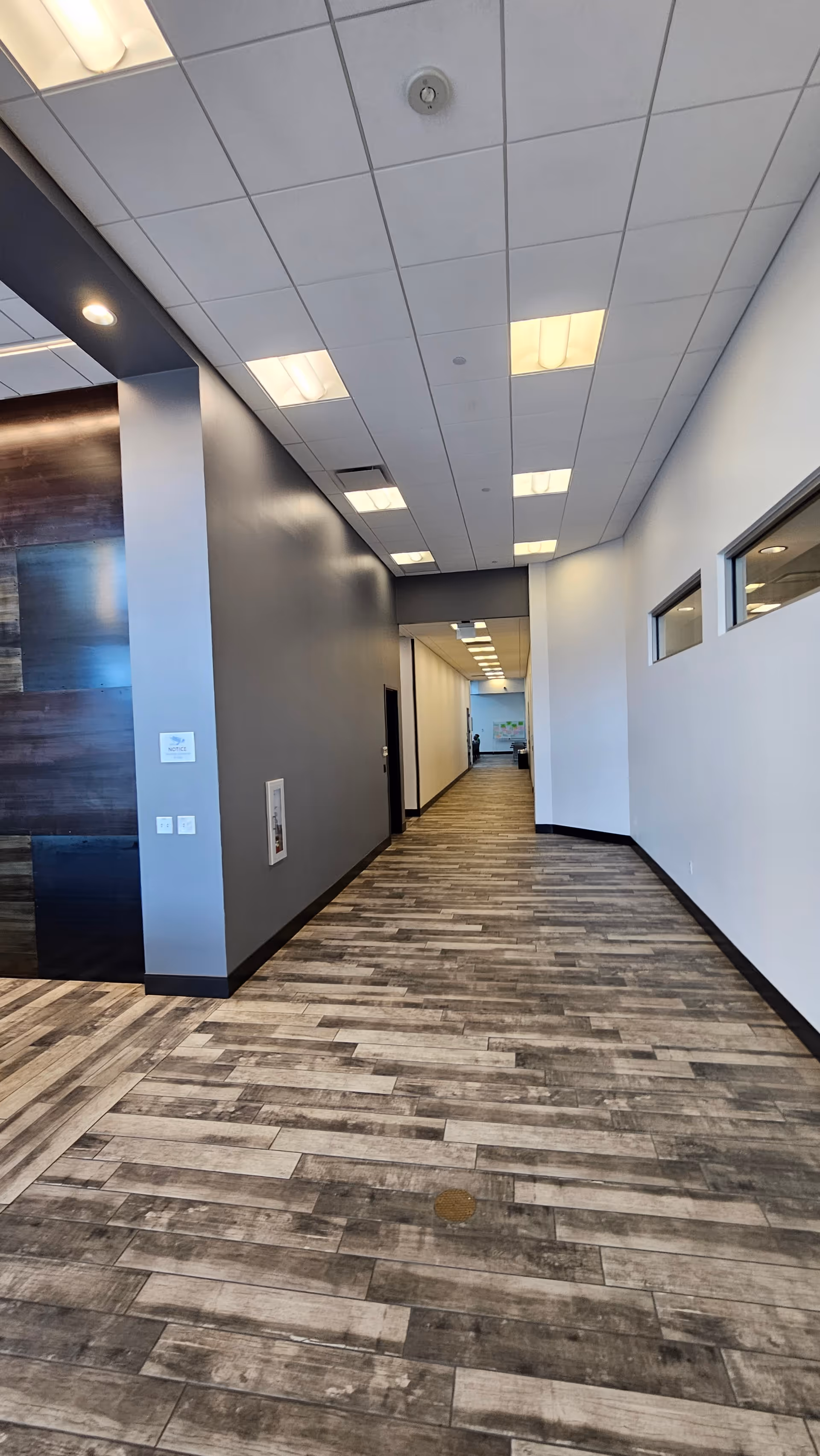 Long modern hallway inside a facility with wood-like flooring and recessed ceiling lights.