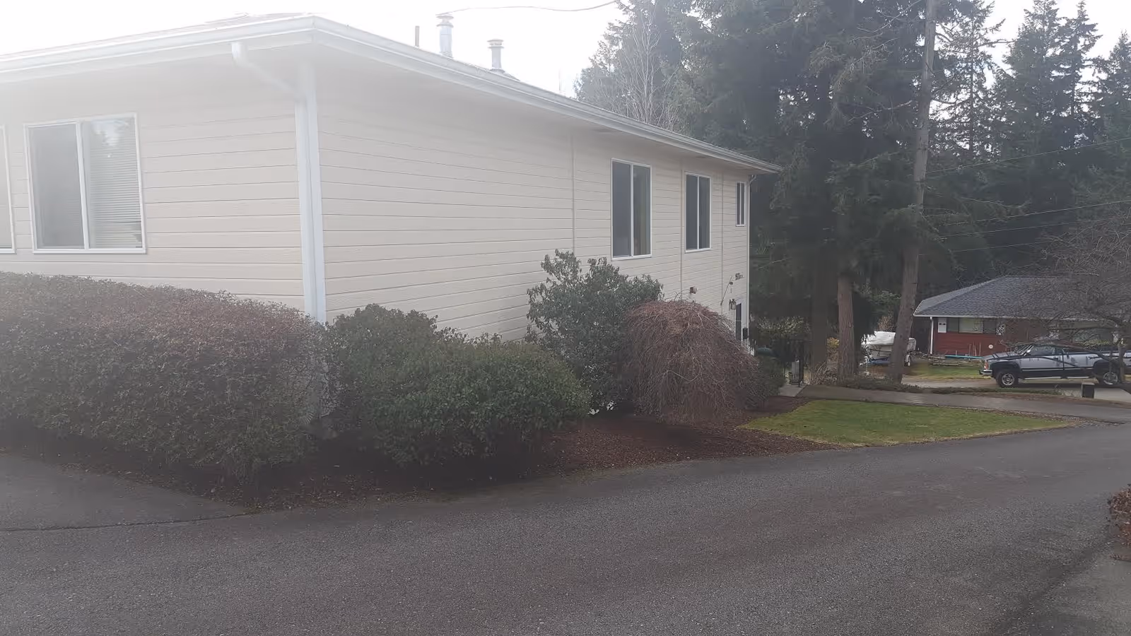 Exterior view of a single-story senior care facility with shrubs and parked cars nearby.