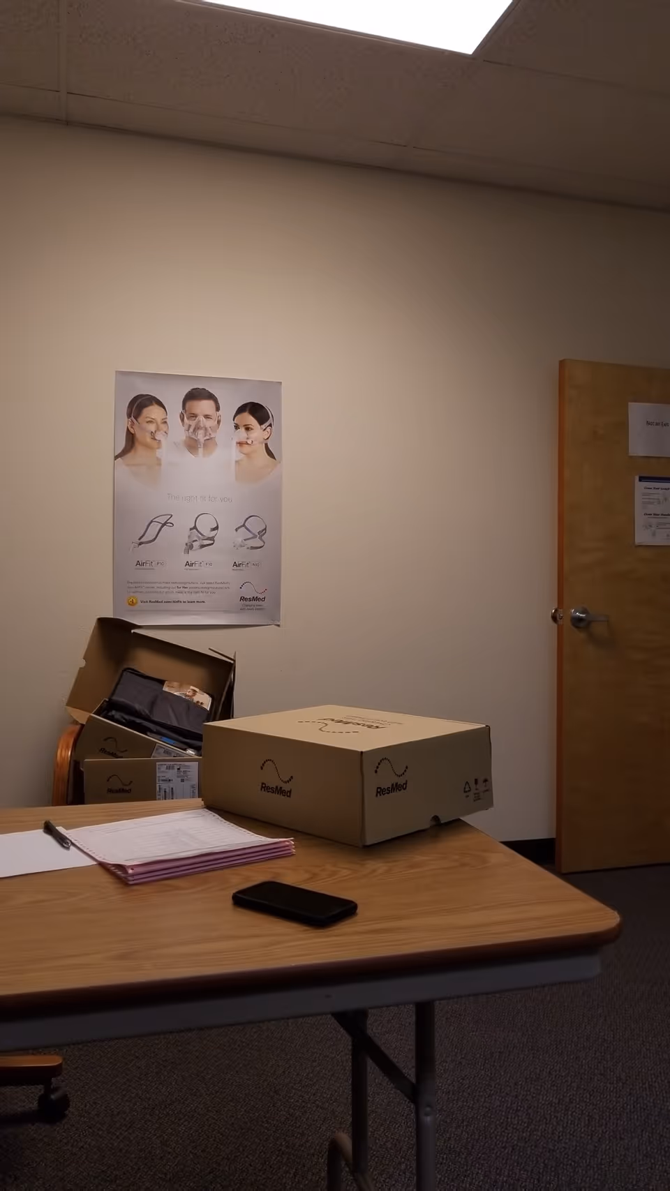Office or break room with desk, boxes labeled ResMed, and a wall poster.