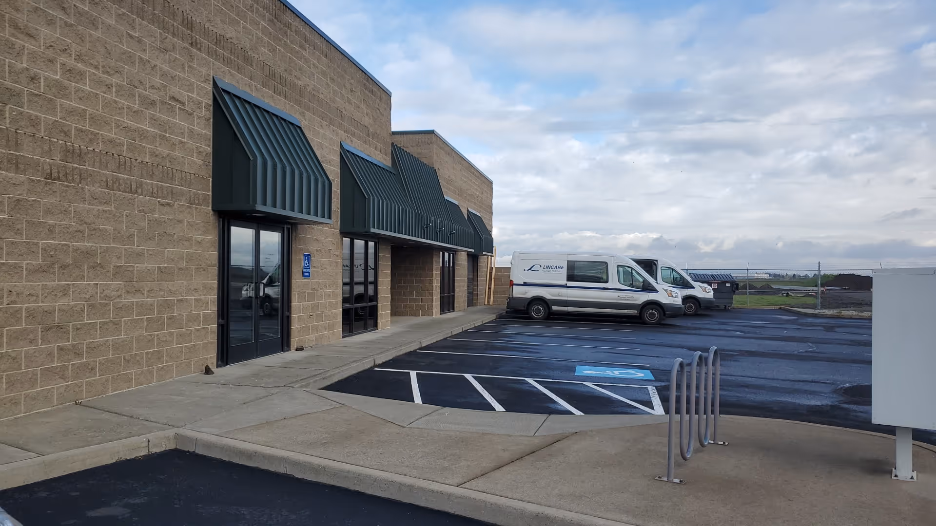 Exterior view of a tan brick senior facility with two white LINCARE vans in parking lot.