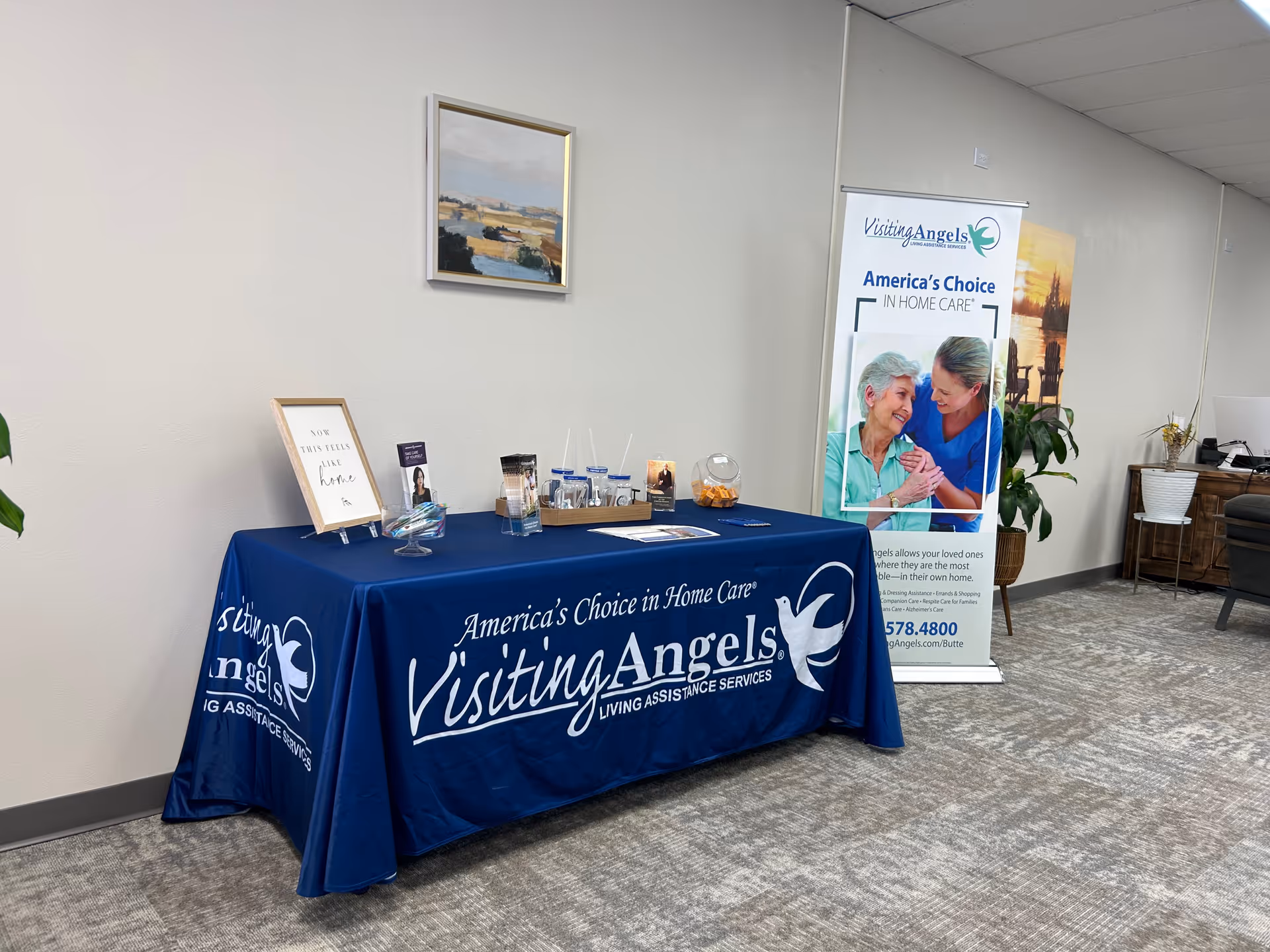 Indoor reception area with a blue Visiting Angels table and promotional banner.