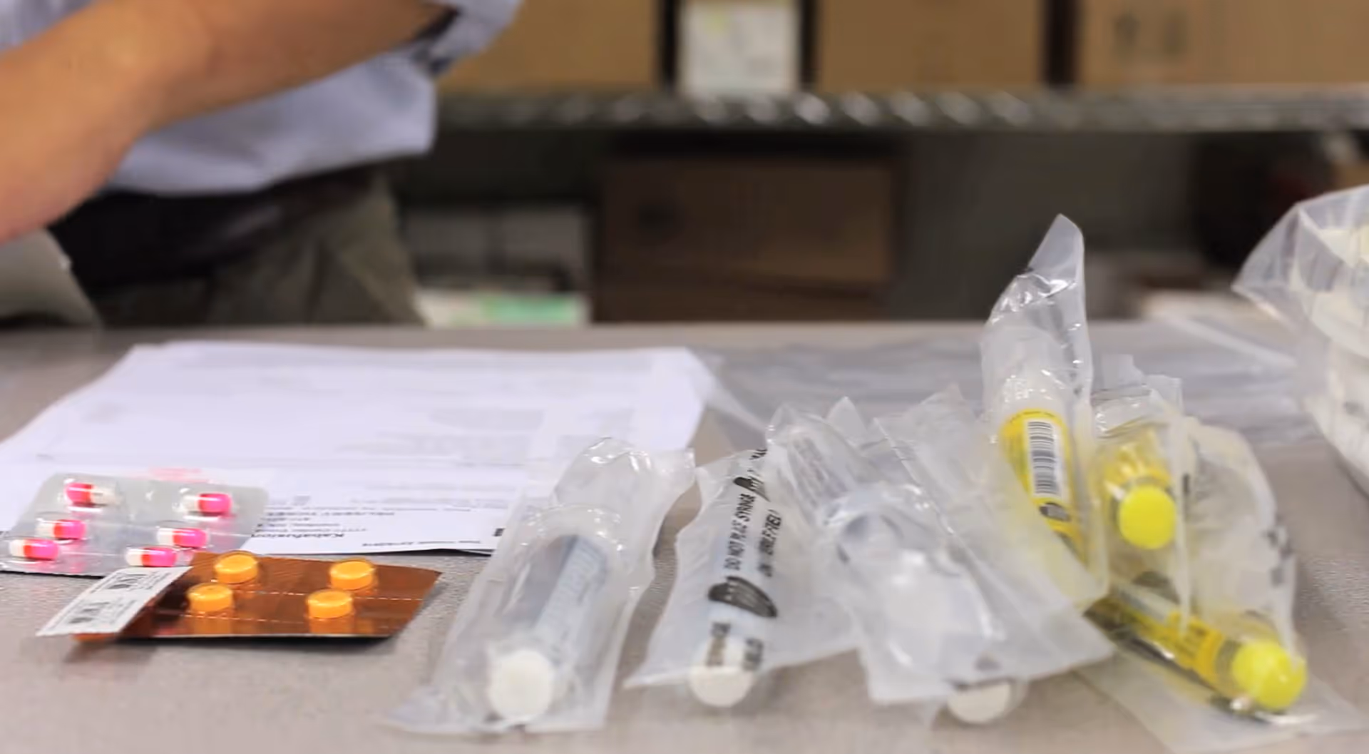 Close-up of assorted syringes and pills in blister packs on a counter at a care facility.