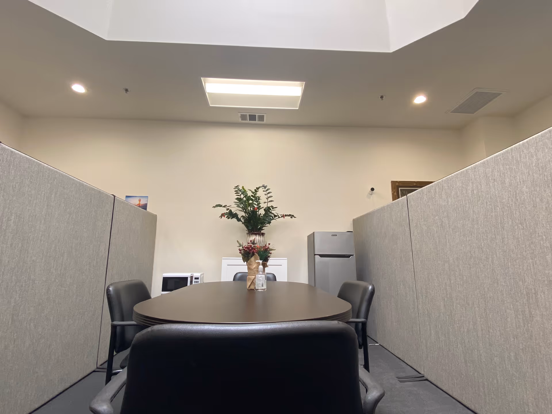 Round table with black chairs in a cubicle-style conference room, centerpiece plant.