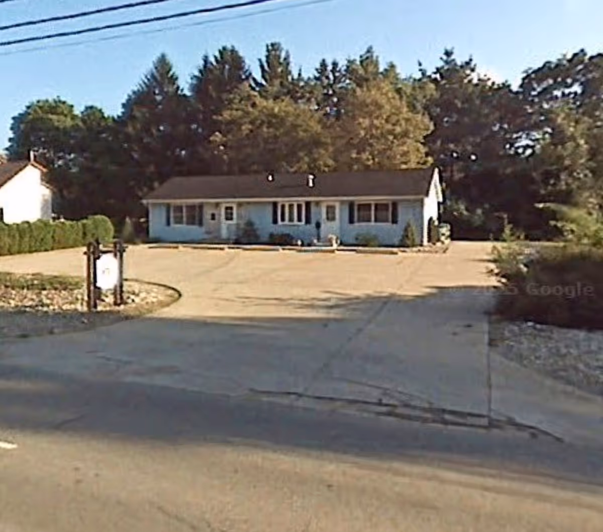 Front view of a single-story light-blue facility with a driveway and surrounding trees.