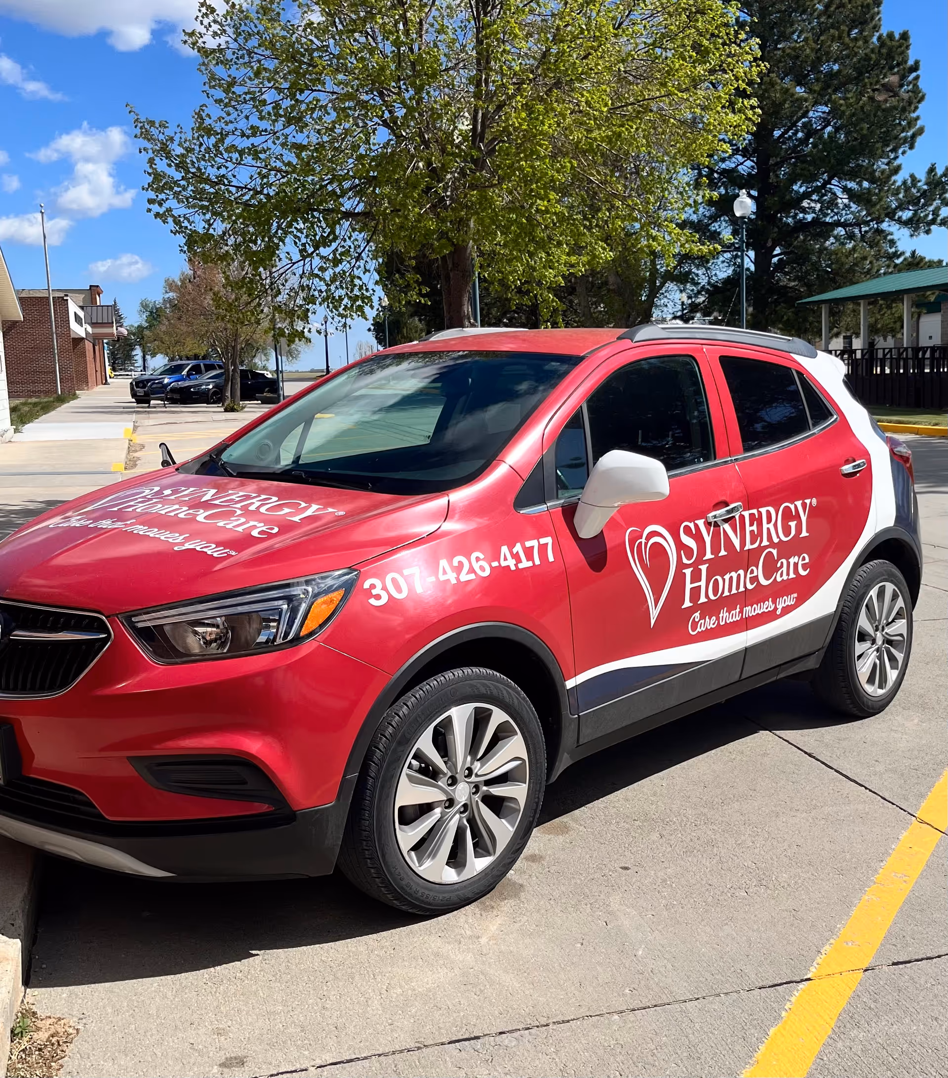 Red Synergy HomeCare van with logo parked in a sunny outdoor lot.