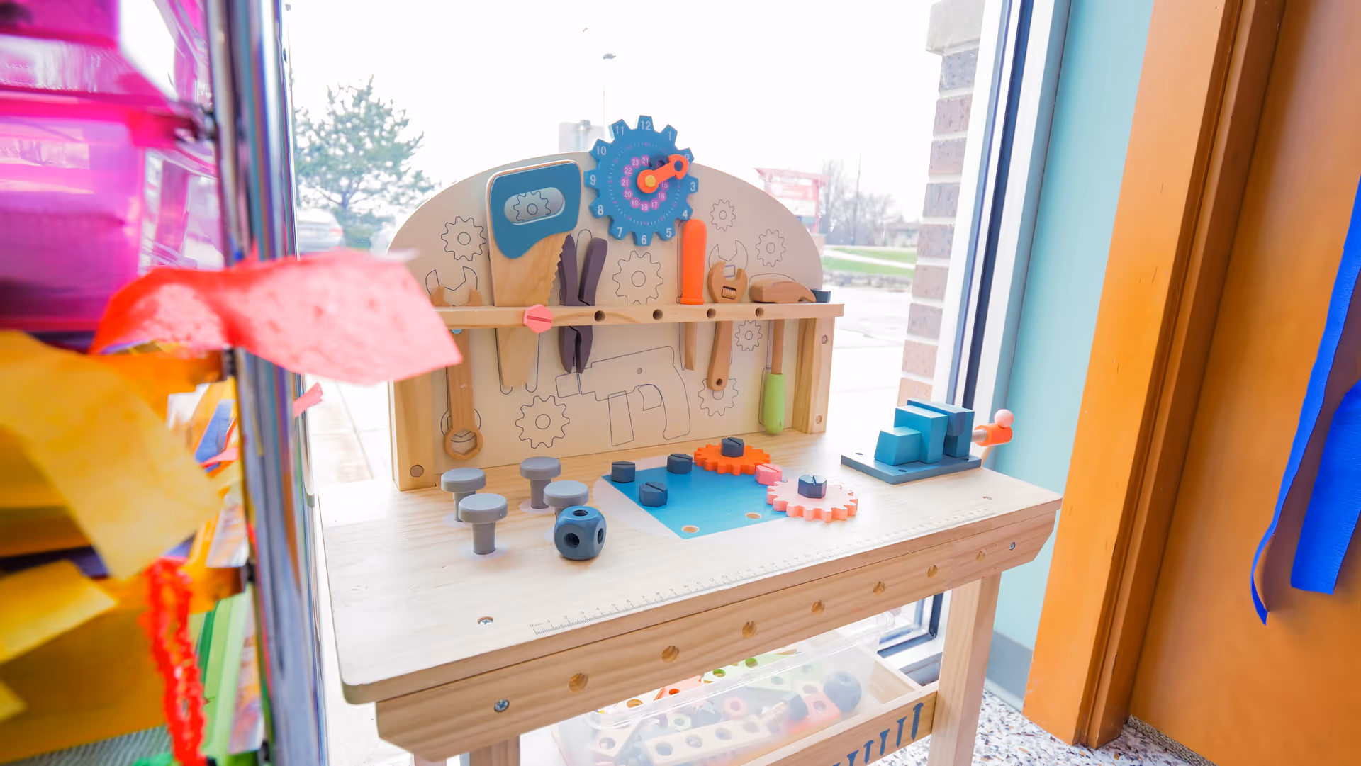 Child-friendly wooden activity table with gears and shapes near a window in a bright room.