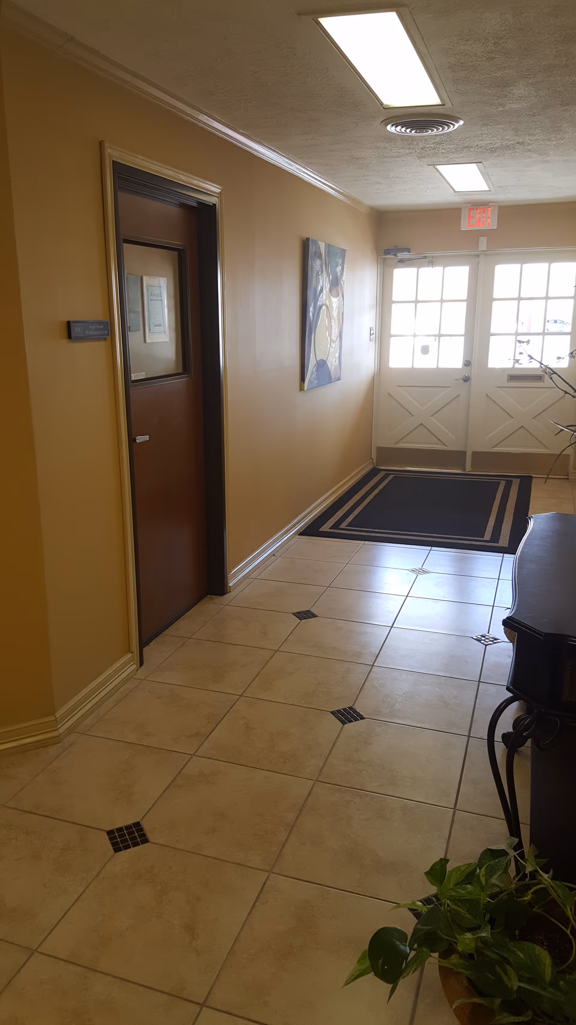 A beige hallway in a senior living facility with doors, artwork, and tiled floor.