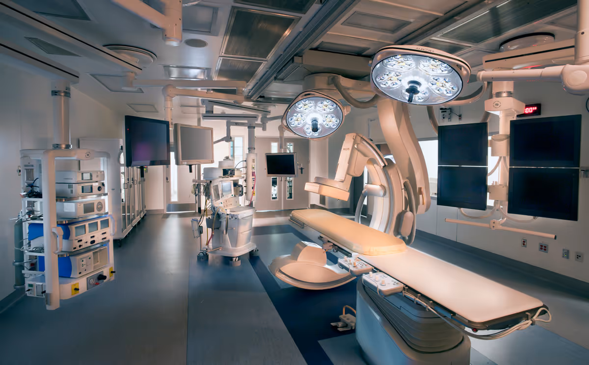 A modern hospital operating room with surgical table, overhead lights, and medical equipment.
