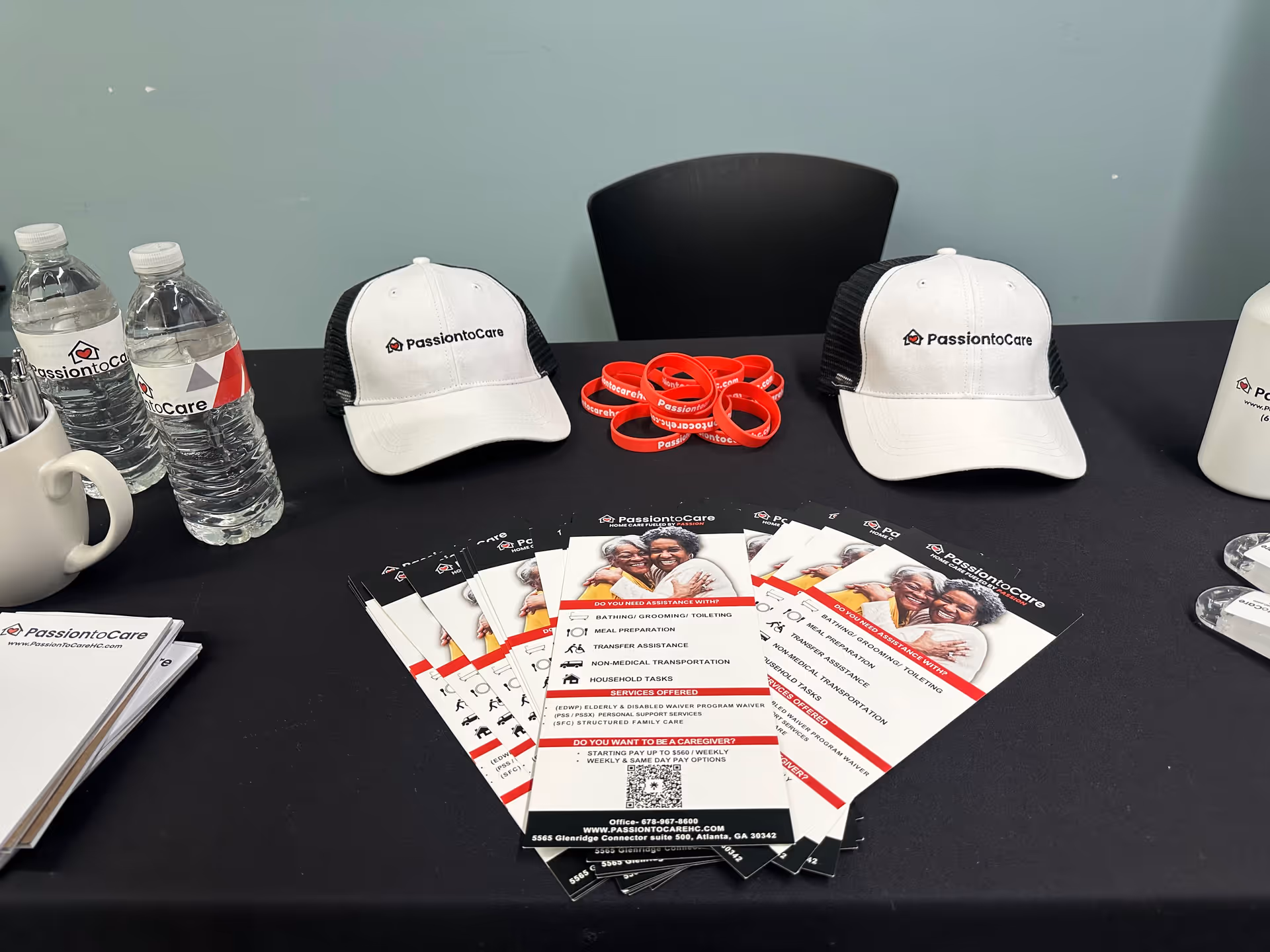 Promotional display on a table with PassiontoCare hats, brochures, and water bottles.