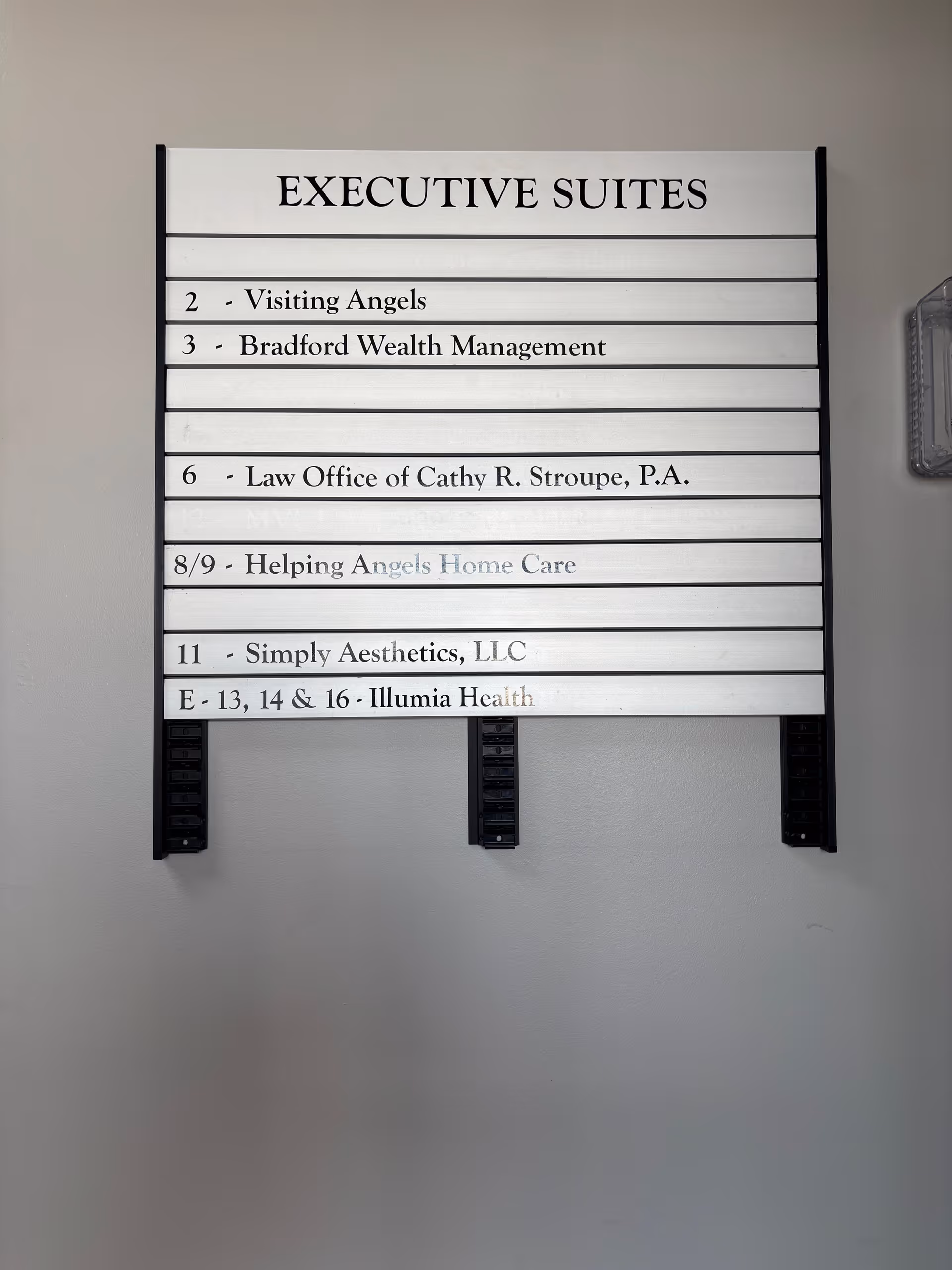 Directory sign reading EXECUTIVE SUITES lists tenants like Visiting Angels on a gray wall.