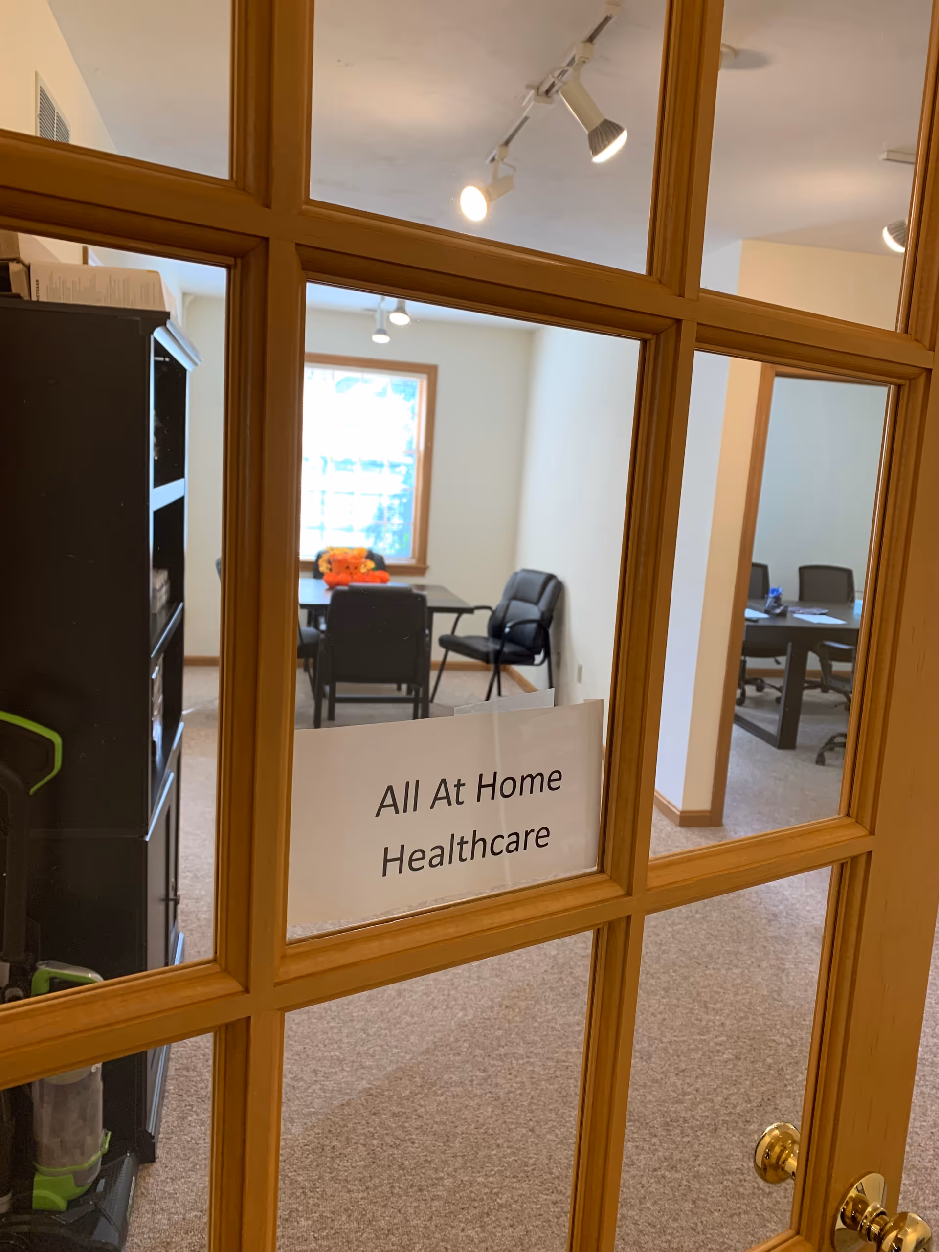 Glass-framed wooden door with a sign reading All At Home Healthcare; interior conference room beyond.
